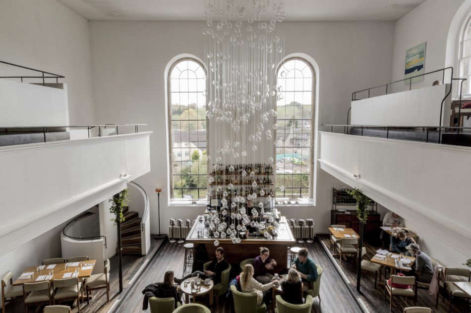 The double-height dining room is illuminated by a cascading glass fiber optic chandelier by Bruce Monro. The owners enlisted architects Mackenzie Wheeler to oversee the rehabilitation of the building. Photograph courtesy of The Modern House.