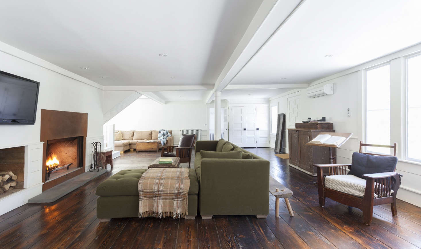 The open-plan living room/family room/dining room has its own steel-front fireplace and original wide-plank floors. The wainscoting and ceiling coffers were built from pine trees felled and milled on the property. The living room is painted in Benjamin Moore’s Decorator’s White. “My trifecta is White Dove, Decorator’s White, and Super White,” says Givone about his favorite Benjamin Moore paints.