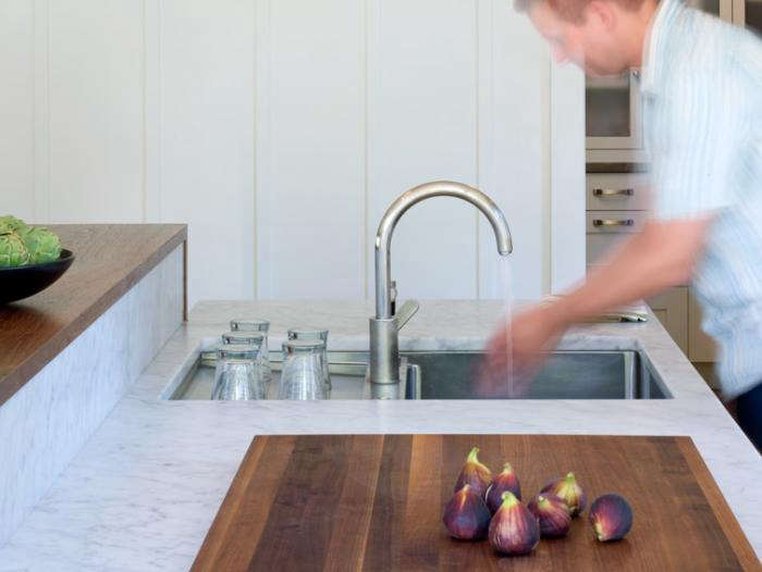 In this Indoor/Outdoor Kitchen, Buttrick created a custom stainless drain board behind the sink, which frees up the area on either side. The marble recessed backsplash is built into the raised walnut counter that sits six inches taller than the marble counter, concealing the work area from guests but still making it visually gratifying for guests on the other side.