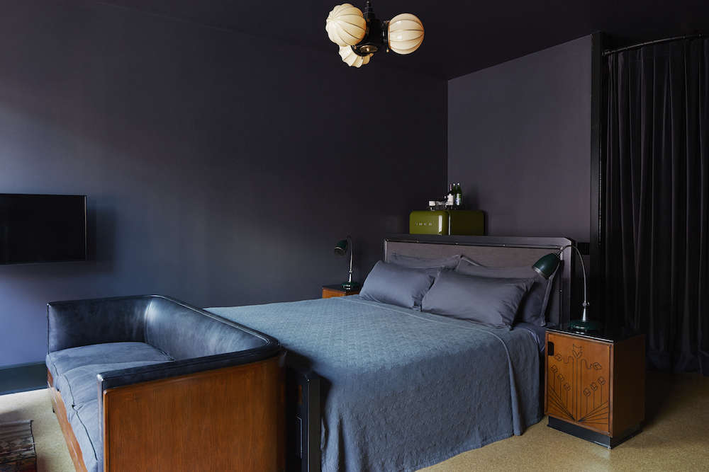 Every Ace Hotel sports a custom signature blanket; this one is a lightweight cotton matelassé coverlet in a pattern inspired by 1920s French art. A full-size Smeg refrigerator in the corner serves as an oversize mini-bar. A flatscreen TV hangs in every room but recedes against the dark decor.