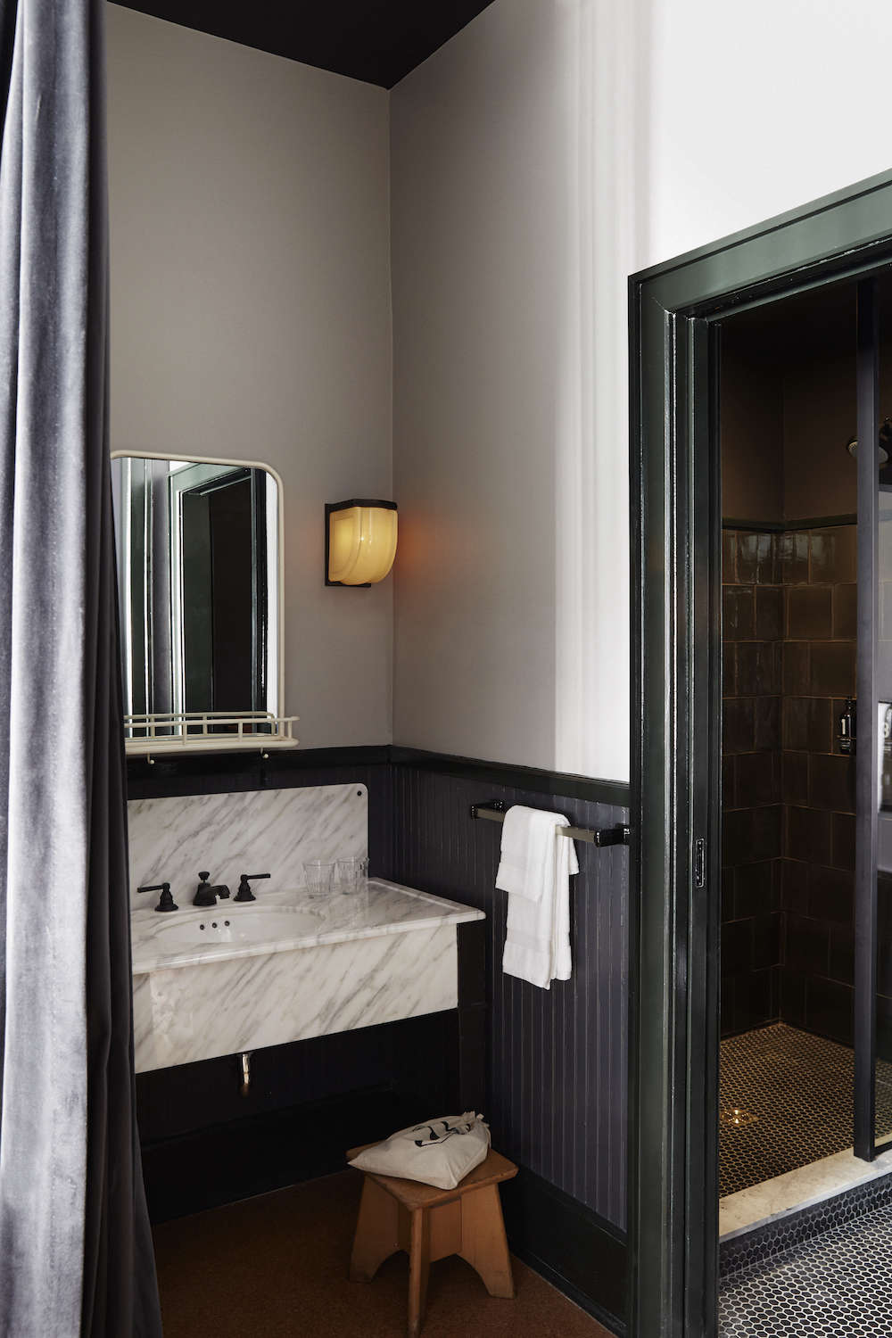 The washroom is hidden by a purple velvet curtain and features custom fixtures and lighting by Roman & Williams. The bathrooms are stocked with soap from Pearl+ and toiletries by Rudy’s Barbershop.