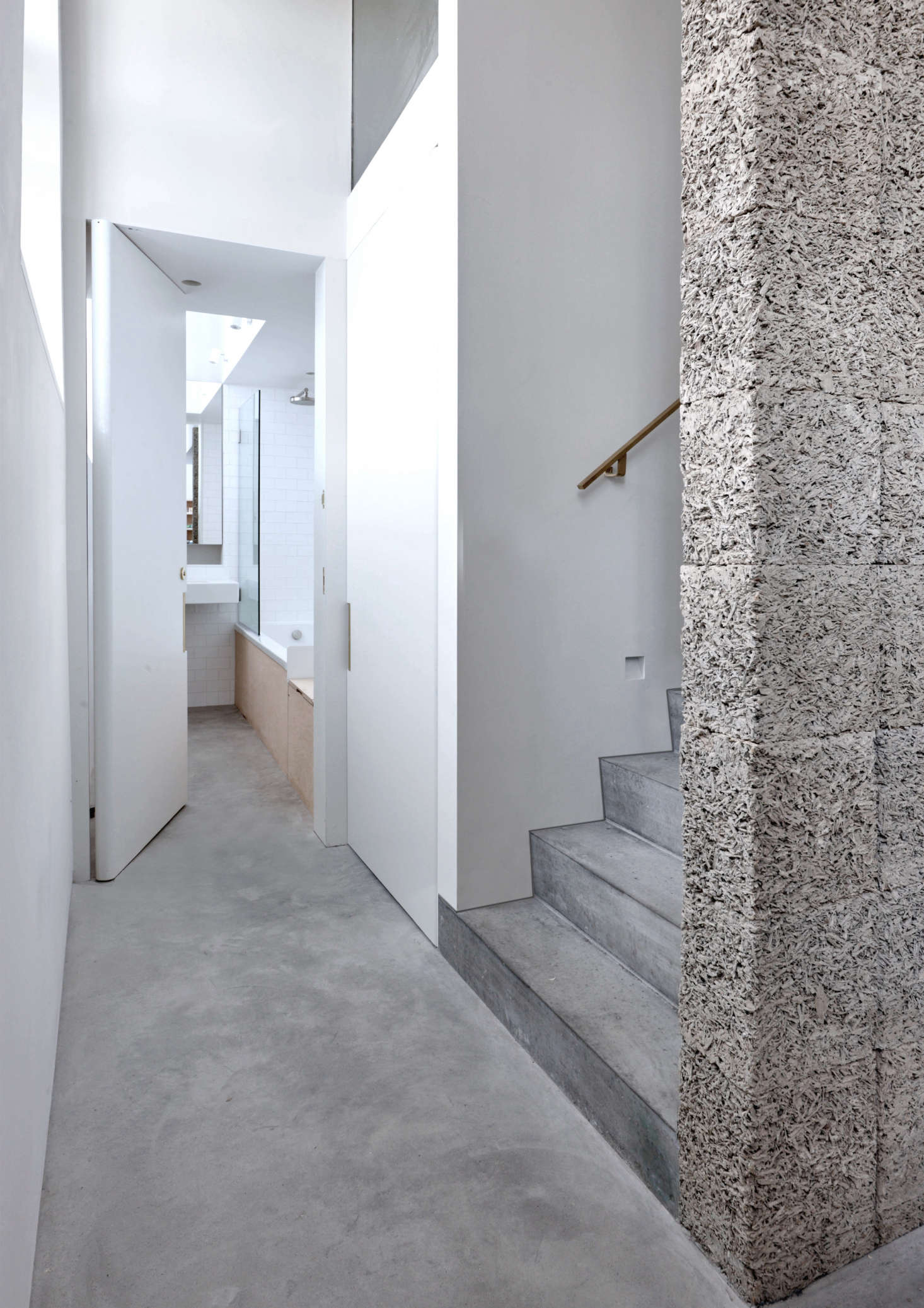 Another version of recycled wood-cement appears as the dramatic structural spine of the stairs. Also shown, a glimpse of the skylit downstairs bath, where polished concrete and plywood meet white tiles and glass.