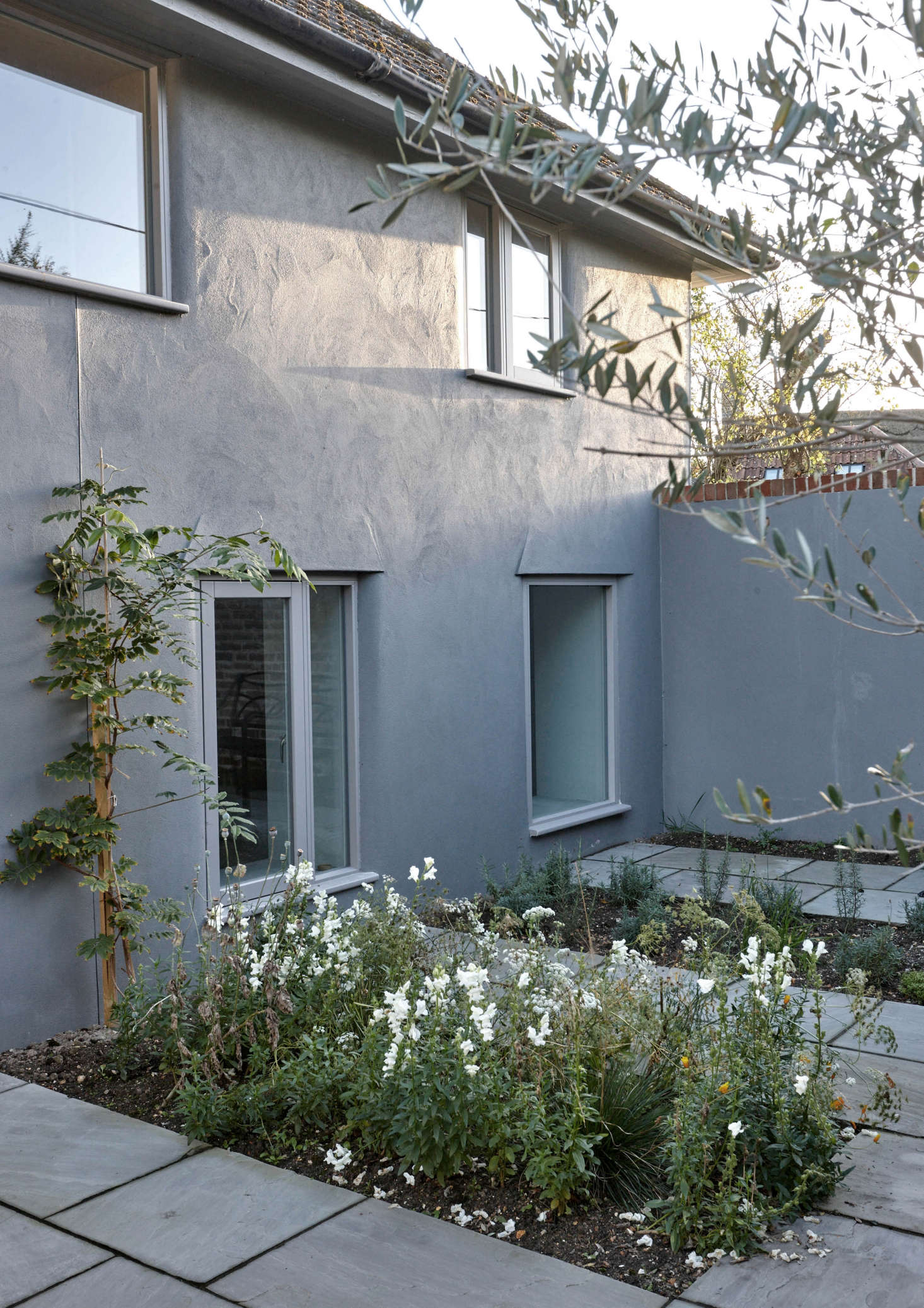 The exterior of the old school was also overhauled. Though the roof was left as is—”cement tiles from the 1980s, not worth focusing on,” says McLaren—all-new windows were introduced and the walls were lime rendered and painted, a traditional UK approach that allows the building to breathe. A slate terrace with plantings now leads to the front door.