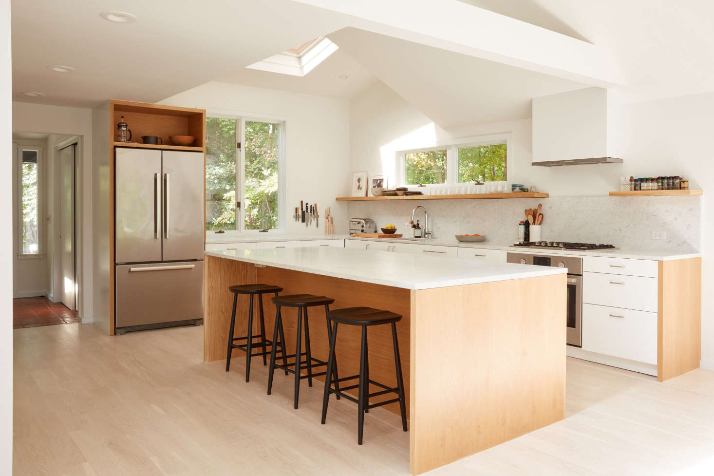 In addition to removing the kitchen wall, Jones and team lofted the ceiling. (The skylight was original—the ceiling was “a strange mix of different heights,” Jones says.) Jones sourced the white Ringhult cabinets from Ikea and added custom oak open wood cabinets and shelves. The Carrara marble counters are sourced from ABC Stone in Brooklyn. The fridge, oven, and cooktop are all Bosch; the vent hood is Miele. The black stools are Ercol stools from A+R in LA.