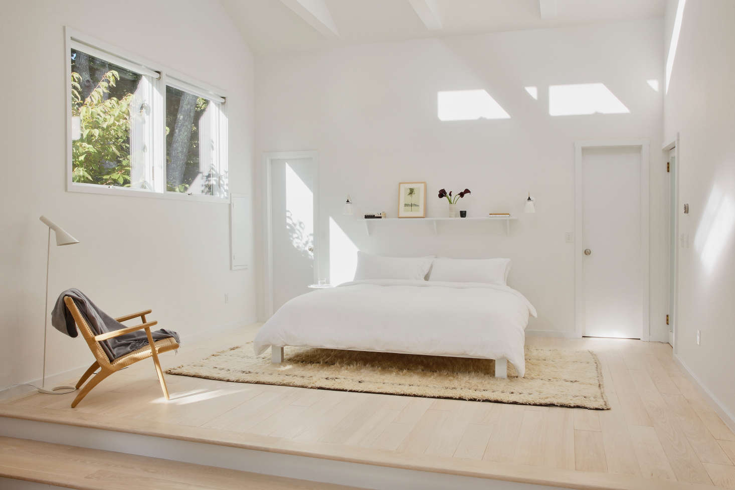 “Throughout the house, the palette we chose is oak wood and white paint,” Jones says. “We wanted to keep it very simple with light, natural materials.” Case in point: The master bedroom. Jones took down a half wall separating the bedroom from a sunken lounge, and added a Hans Wegner chair, another Moroccan Beni Ourain rug from Etsy (here’s a similar option), a white standing lamp by Arne Jacobsen from Design Within Reach, and Coyuchi bedding from ABC Carpet & Home. Jones doubled the size of the windows next to the bed and added unobtrusive rolling shades from the Shade Store.