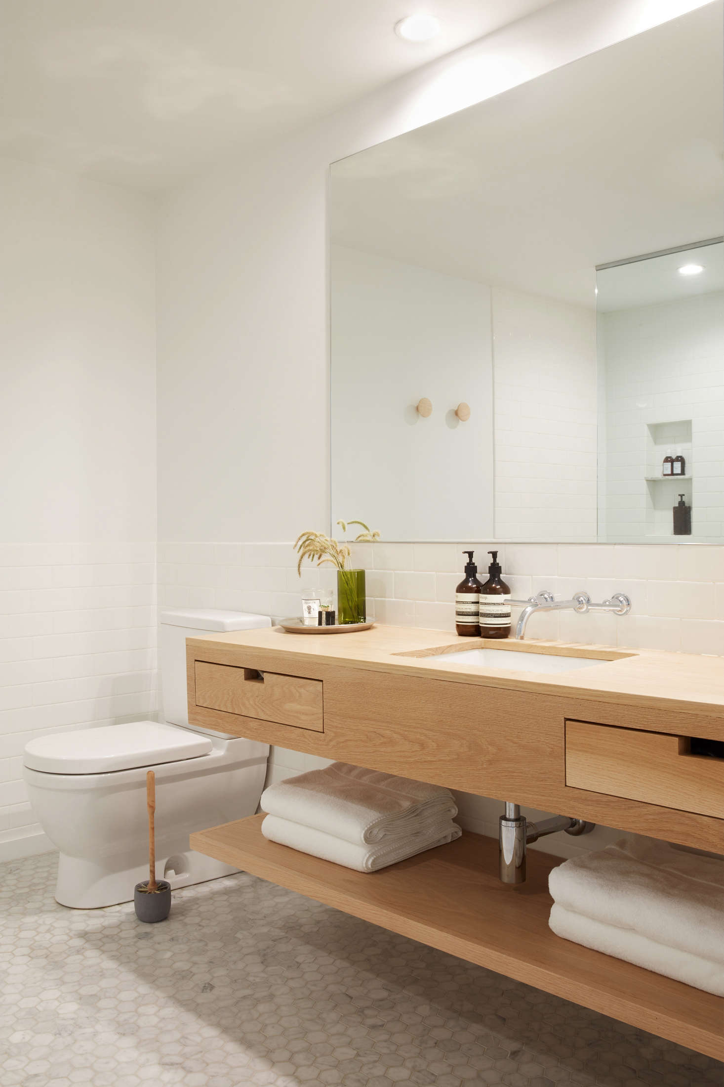 The guest bath is tiled with gray Carrara marble hexagonal tile from Stone Source. The toilet brush and holder are by Iris Hantverk and a green glass vase, from Brooklyn’s Sprout Home, holds stems. Spotted in the mirror: Muuto wooden dots.