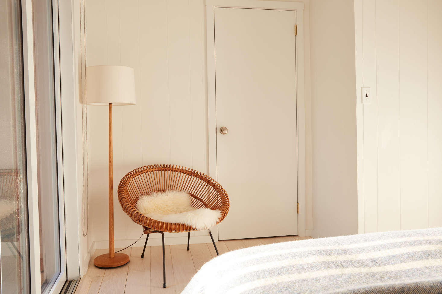 At the foot of the bed: a rattan Franco Albini chair, a Danish standing lamp from Etsy, and the door to an en suite bedroom.