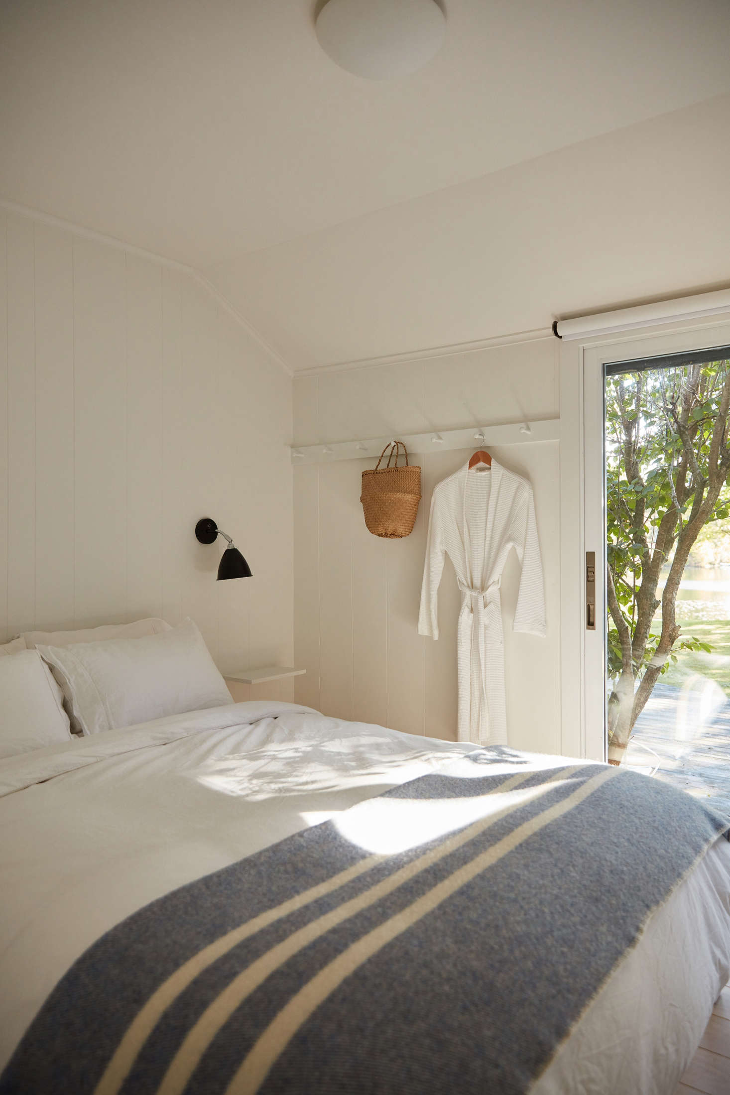 In the first of three guest bedrooms, Jones sourced Shaker pegs from the Container Store and had them fitted to a custom board. The Bestlite black sconces are from Lumens, and the floating shelves were custom-built. The Canadian wool blanket is from Nalata Nalata.