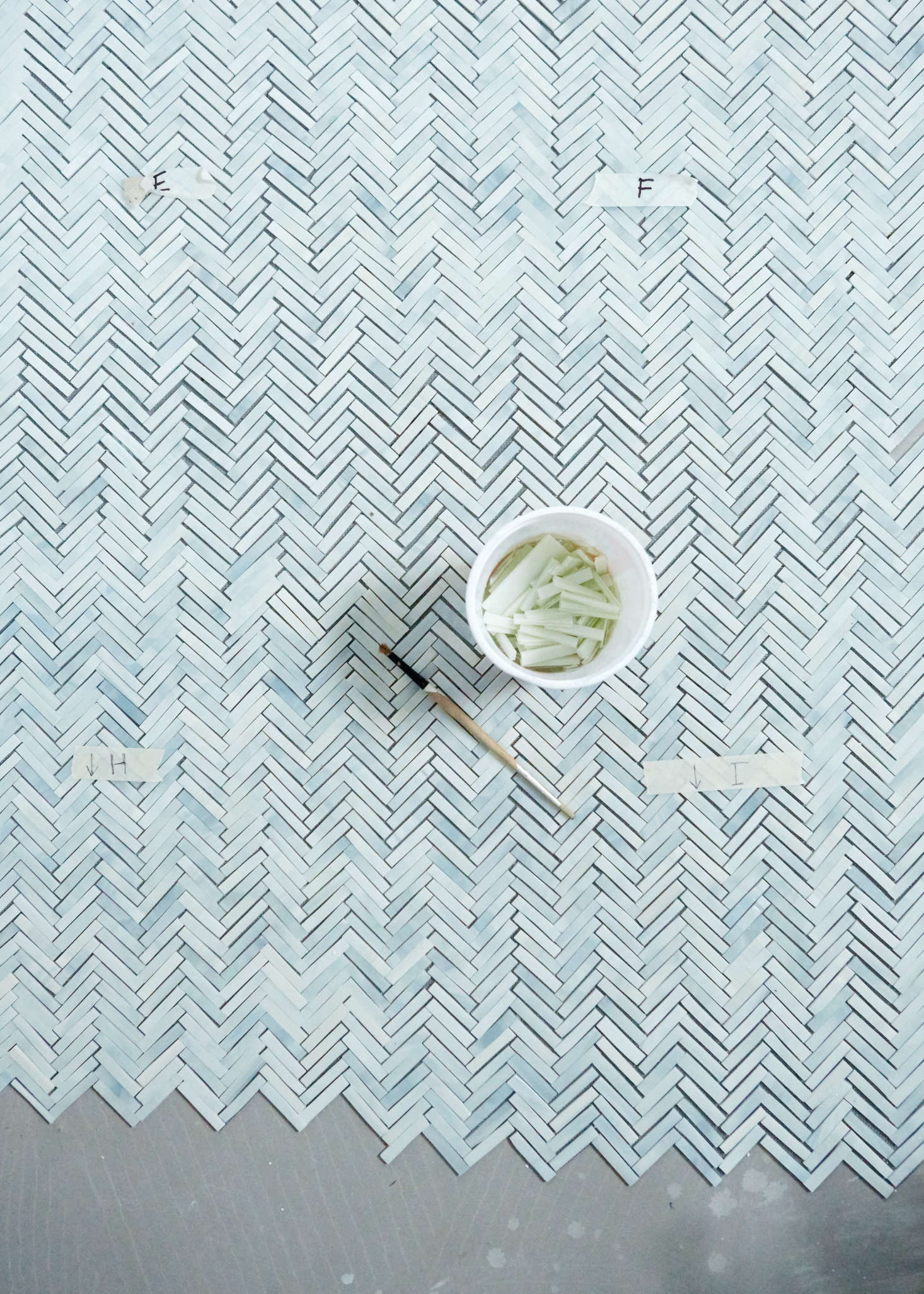 Myers uses a no-VOC industrial adhesive by Eco-Bond to adhere the tesserae to the mesh. Laying the tiles on the concrete mortar bed is what brings out the foggy blue variations in the opal glass. After the tiles are cut, Myers notes that she mixes up the pieces 