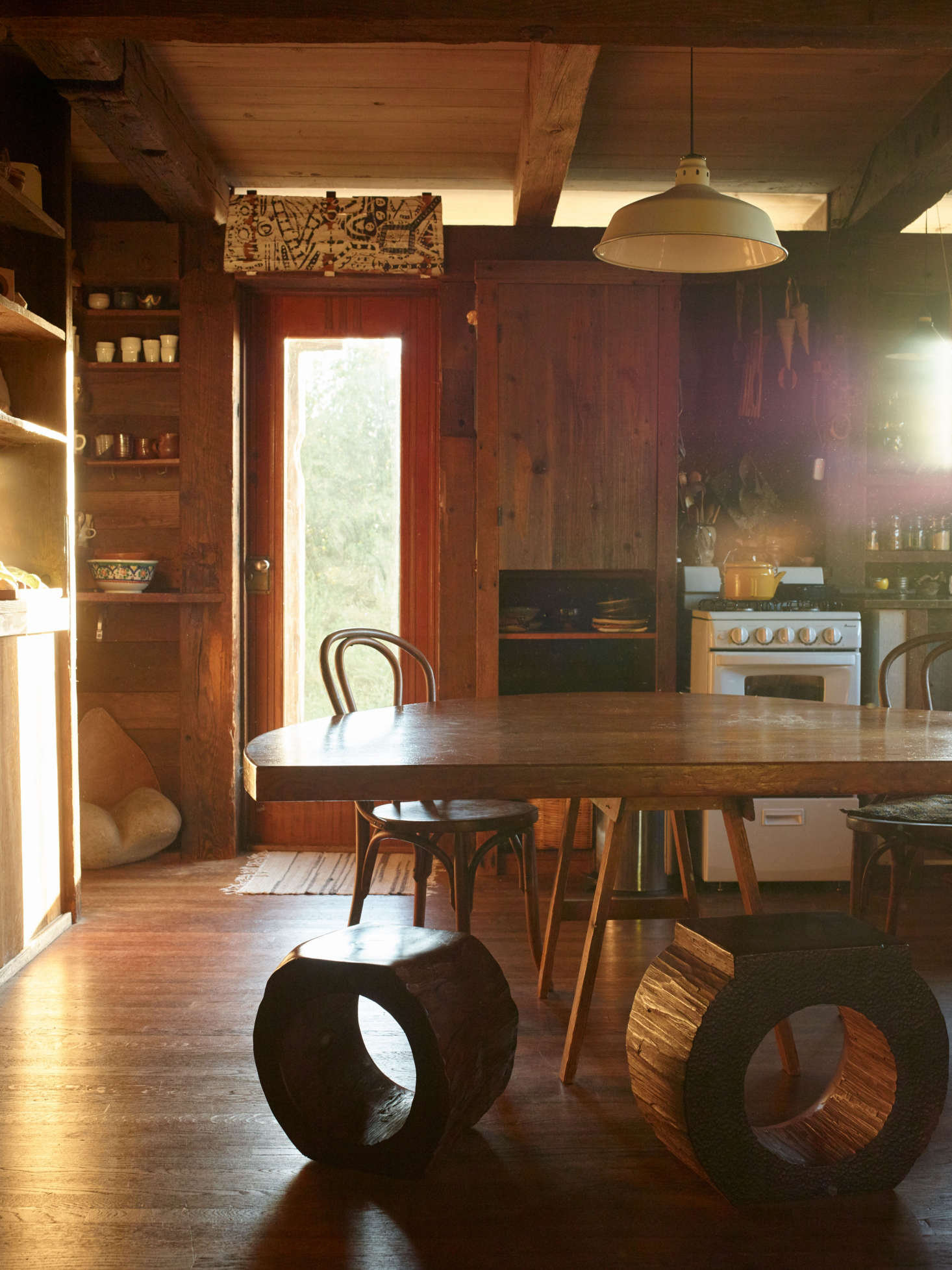 J. B.’s first wife, Nancy Waite, designed and made the kitchen’s polygonal table with sawhorse supports. J. B. hollowed redwood chunks with a chainsaw to make the stools. Above the doorway hangs a Blunk abstract artwork, painted on redwood bark.