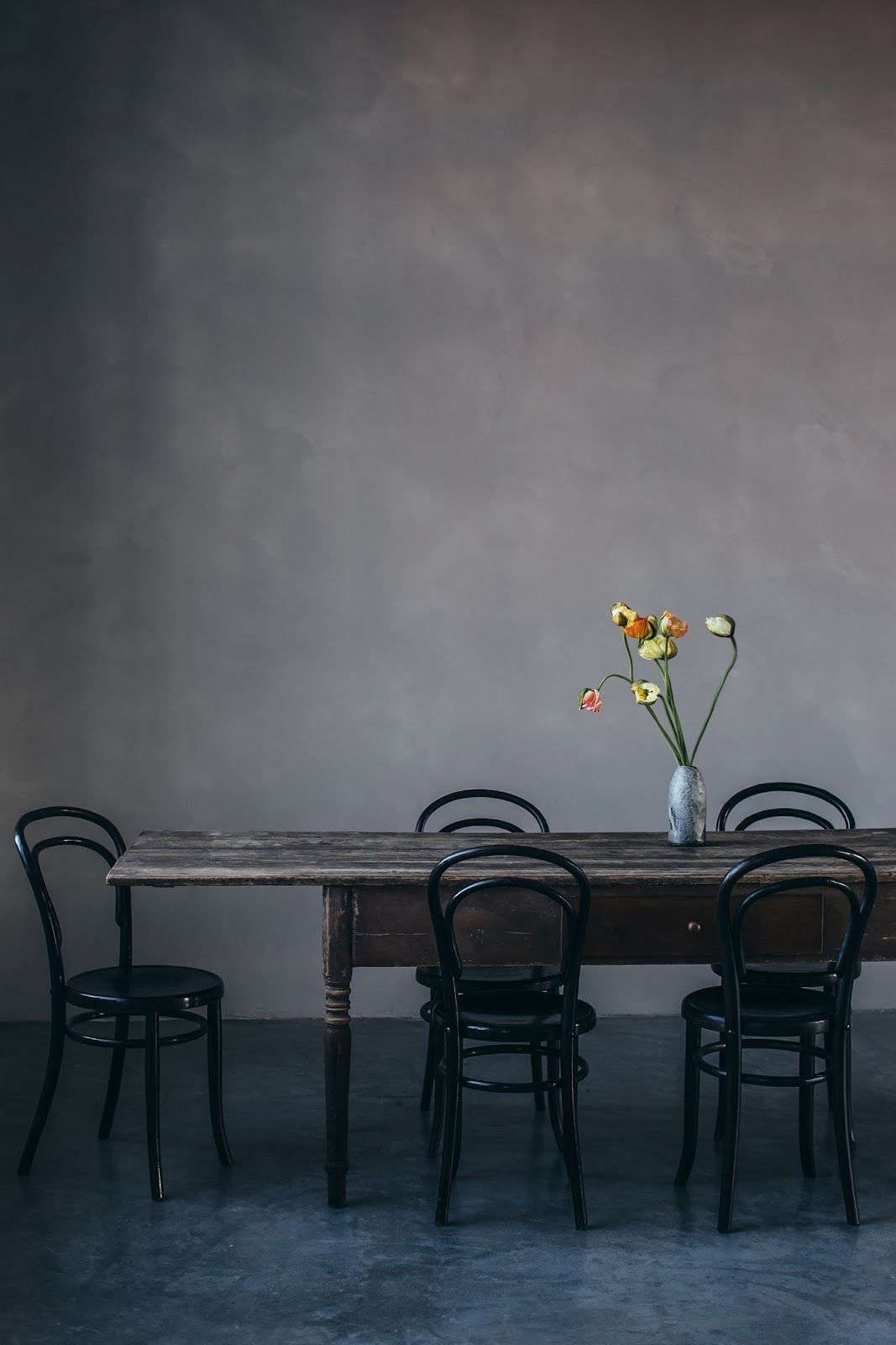 The studio has several dining setups, including this farmhouse table surrounded by vintage Thonet chairs. The mottled gray walls were created using a colored plaster from Kabe of Denmark (here in Concrete).