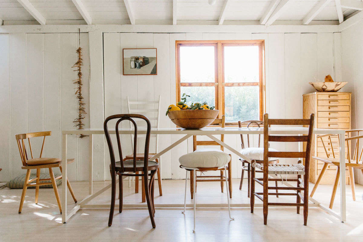 The kitchen opens to a wide, bright dining room, where mismatched wooden chairs—some with oversize cushions—surround the table.