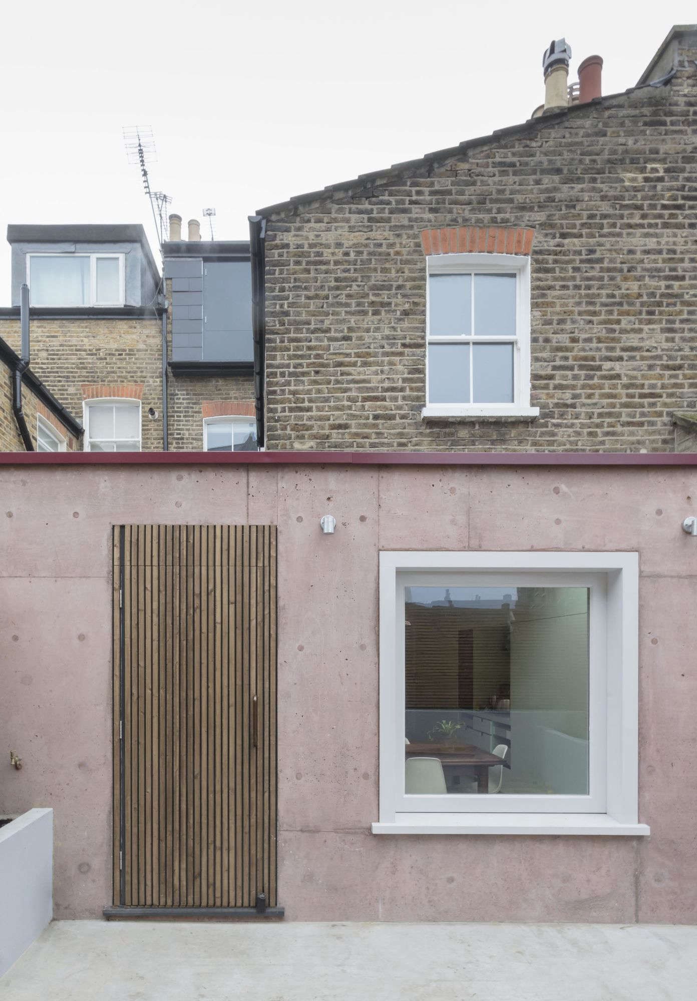 Situated in the back of the house, the six-square-meter (64.5-square-foot) extension features a pigmented cast concrete wall with a slatted wood door and integrated sliding glass window. The new courtyard—shown pre-plantings (it’s now filled with greenery)—is used for outdoor cooking and as a play area.