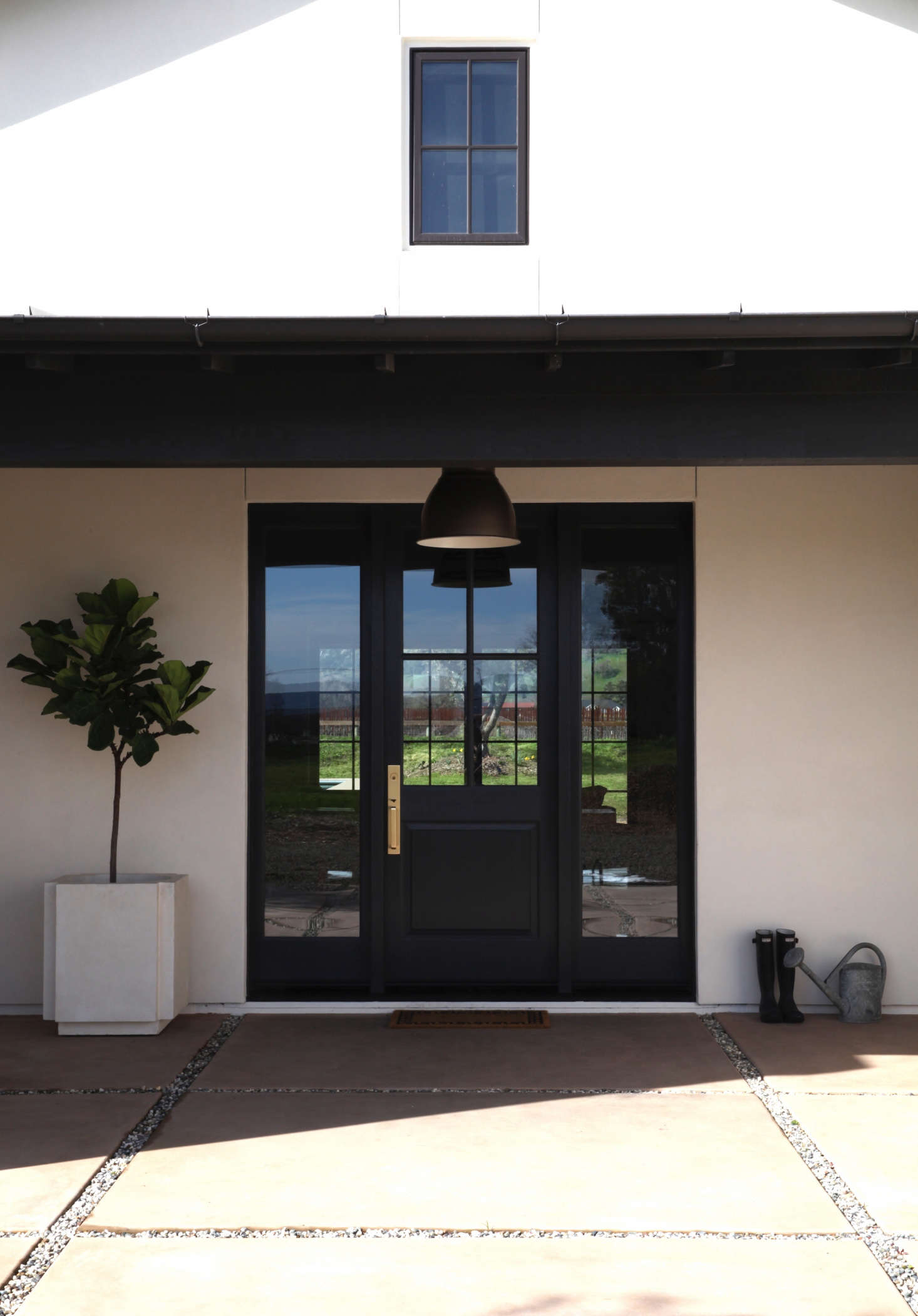 A black Ikea Hektar pendant lamp hangs above the front door. To the left is a fiddle leaf fig tree in a planter by designer Michael Verheyden, available at March.