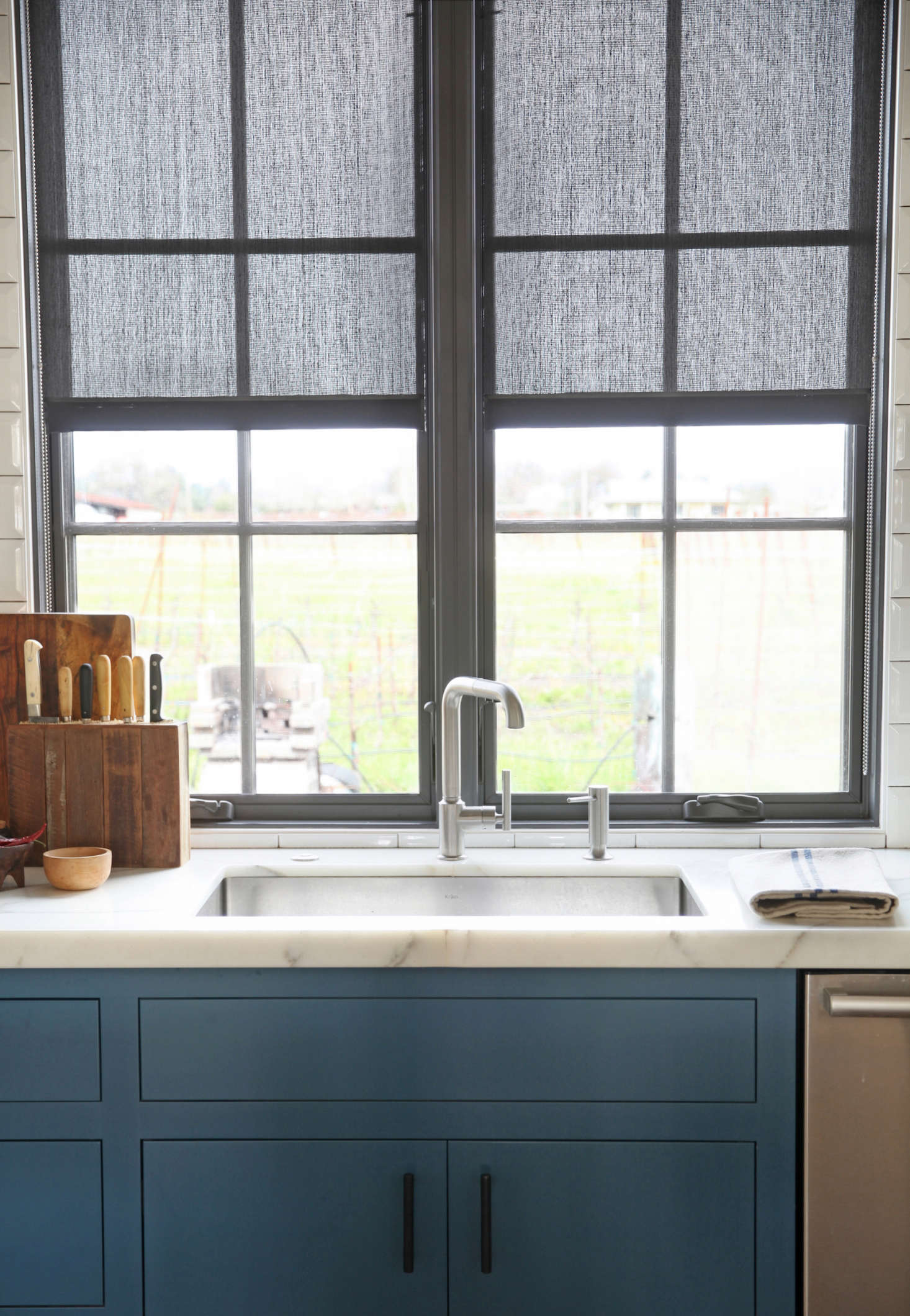 The kitchen window overlooks a view of the environs; landscaping is still in progress. The faucet is by Kohler, the sink is from Kräus, and the countertops are white Calacatta Oro marble.