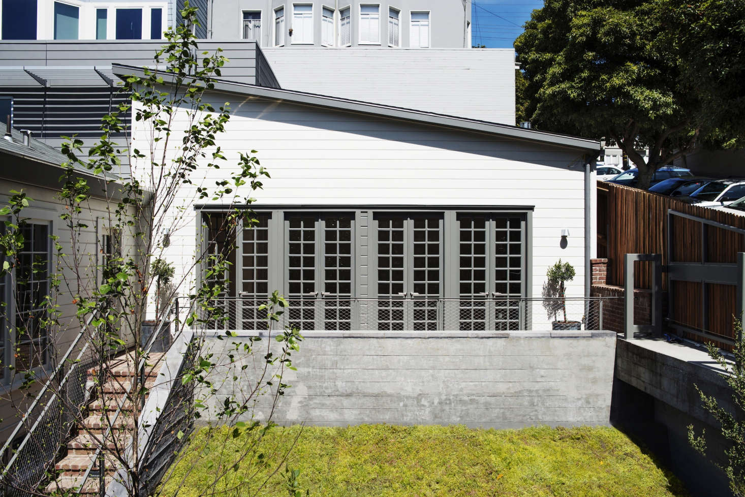 Immediately in front of the first cottage is a car lift linking the street to an eight-car garage beneath the cottages. The lift rises to street level to receive (or deliver) a car through the fence gate, at right. The lift is camouflaged with a green roof of succulents.