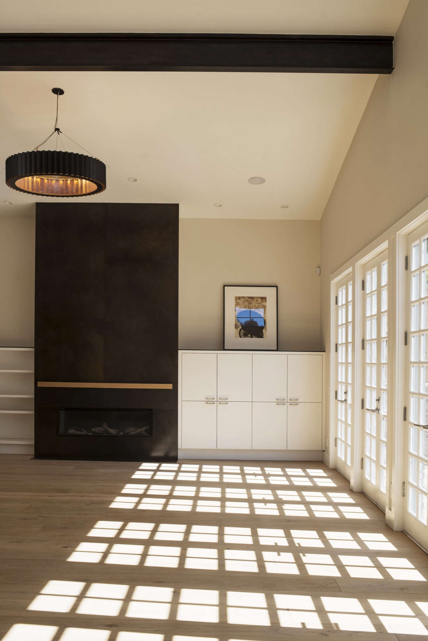 The living room of the streetside cottage has black accents in the fireplace surround, chandelier, and structural I-beam overhead. The light fixture is Gear Suspension from McEwen Studios in Berkeley, and the fireplace surround is a Buttrick design of steel with patina and wax, fabricated by Irongrain in Oakland.