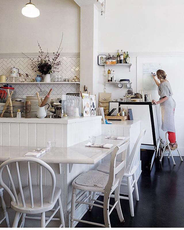 A long, low counter with mismatched white-painted chairs creates dining space around the open kitchen.