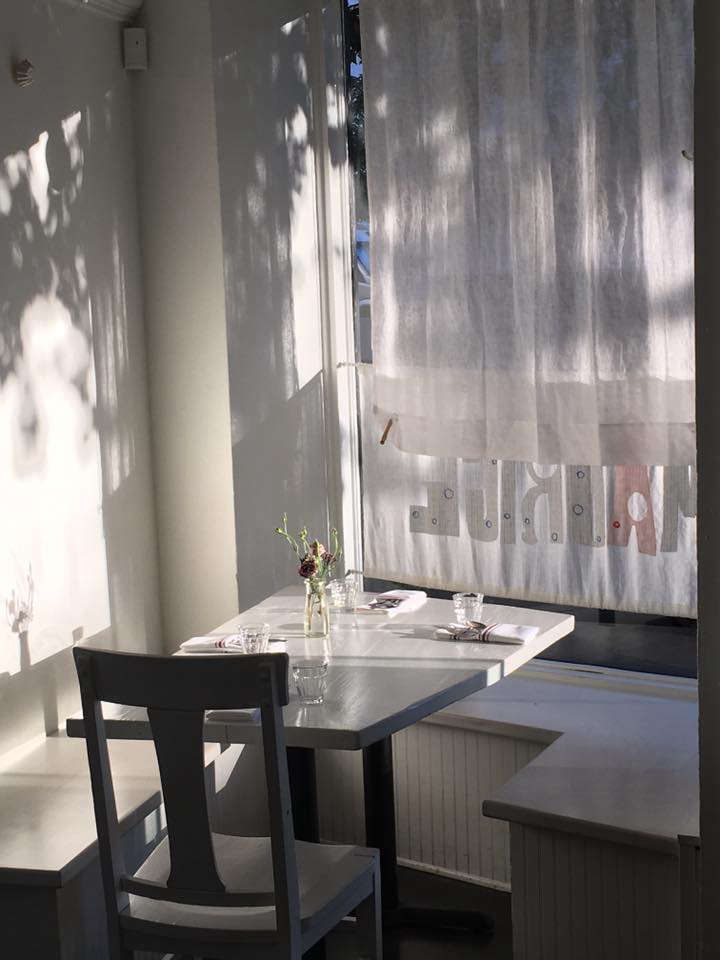 In the front, by the windows, built-in benches maximize seating around small tables. A jar holds freshly-cut flowers.