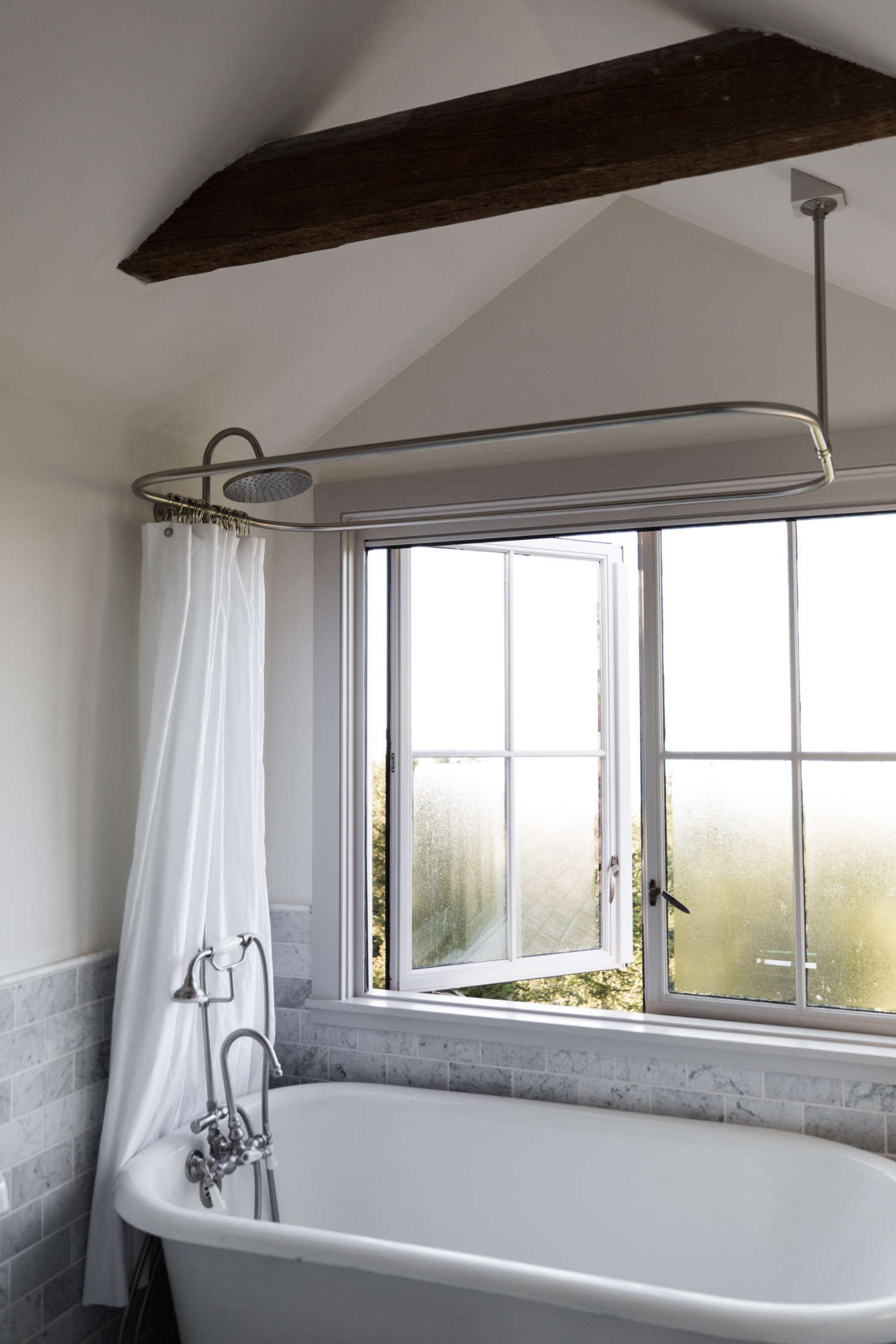 The bath features marble tile and a freestanding bath beneath the original casement windows.