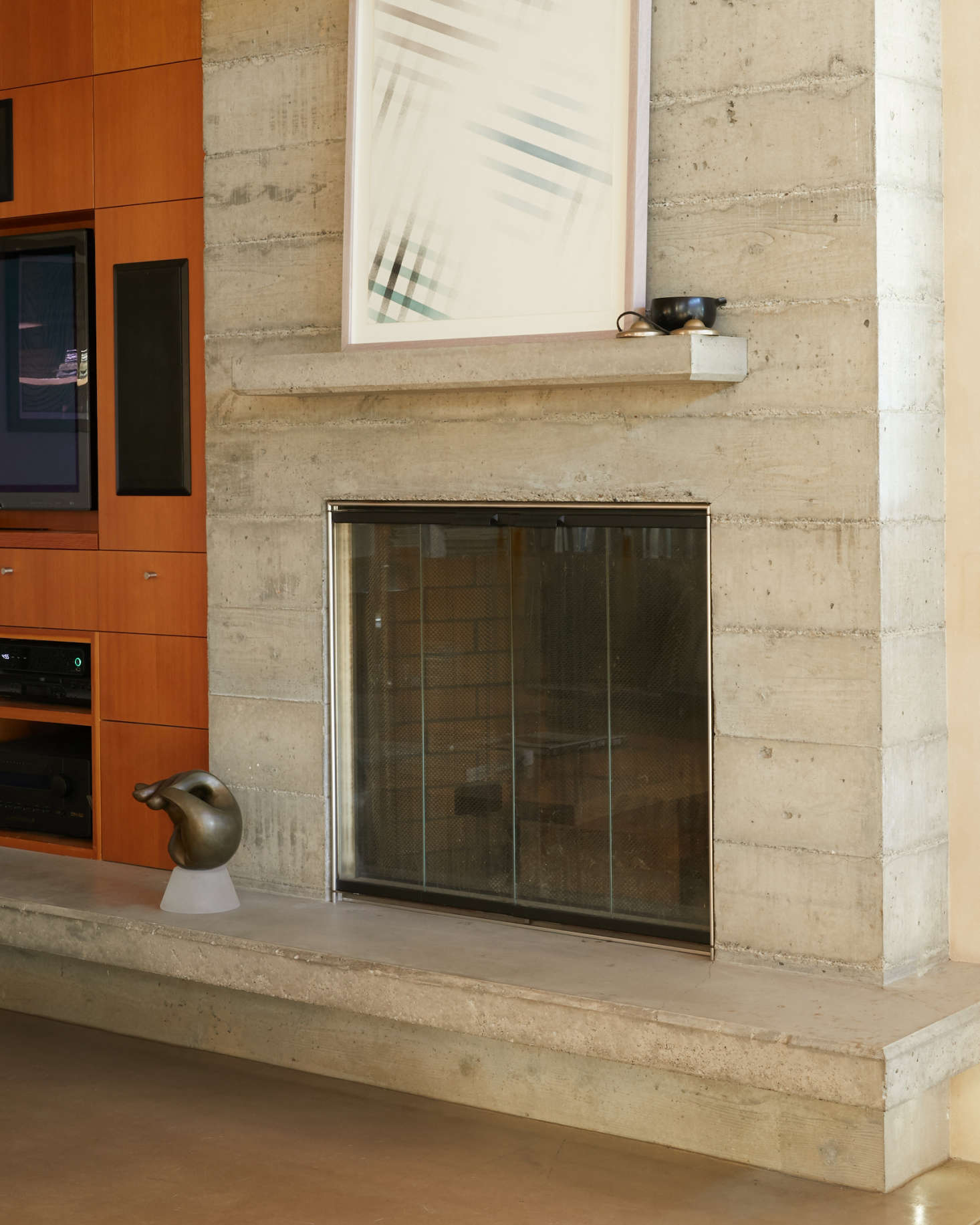 A wood-burning fireplace framed in board-formed concrete at the junction of the dining room and media nook. It