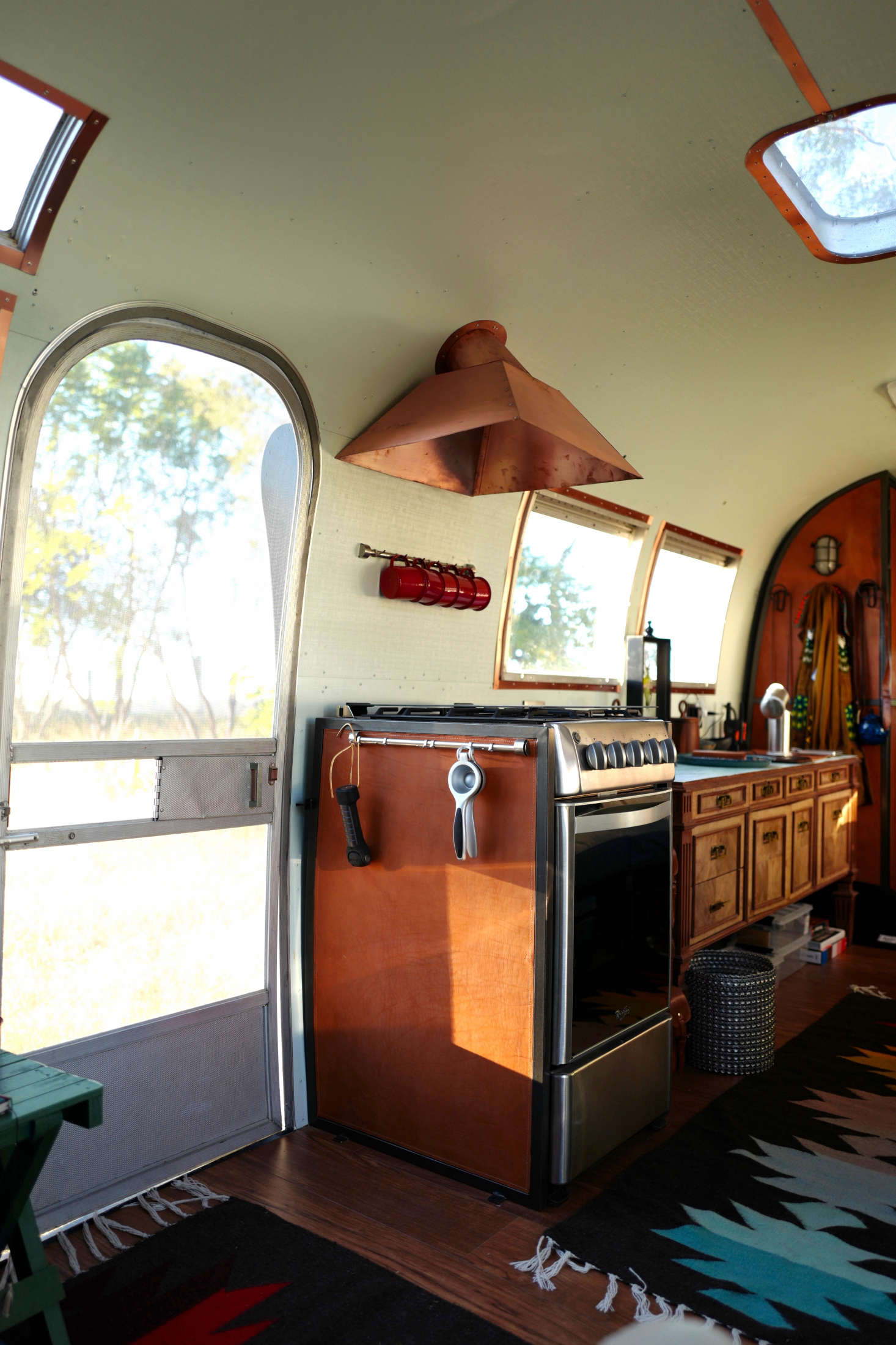 The stove was purchased at a regular appliance store and fitted out with a stitched leather panel on its exposed side. Metal rails are used for hanging mugs and kitchen tools, and the copper hood is custom. A big design decision: whether to include a kitchen sink? Jorge opted to just use the sink in the bathroom: “Having one general sink freed up the counter and made the interior feel more like a studio and not so much a kitchen.”