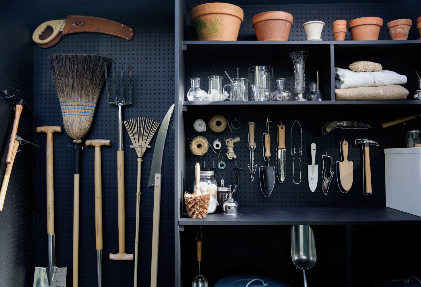 Long-handled tools like rakes and brooms hang on one side of the shed.