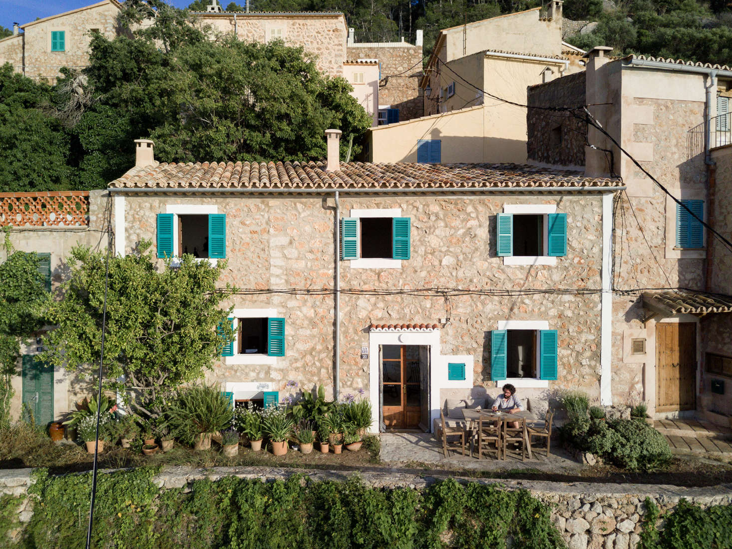 The house’s stately exterior, with a coat of teal-colored paint and a potted-plant garden. The couple has roots on Mallorca: Colón is originally from the nearby town of Esporles and, since moving to Madrid for architecture school in 2001, “had been always looking for a house with sea view in this part of the island,” Palencia says.