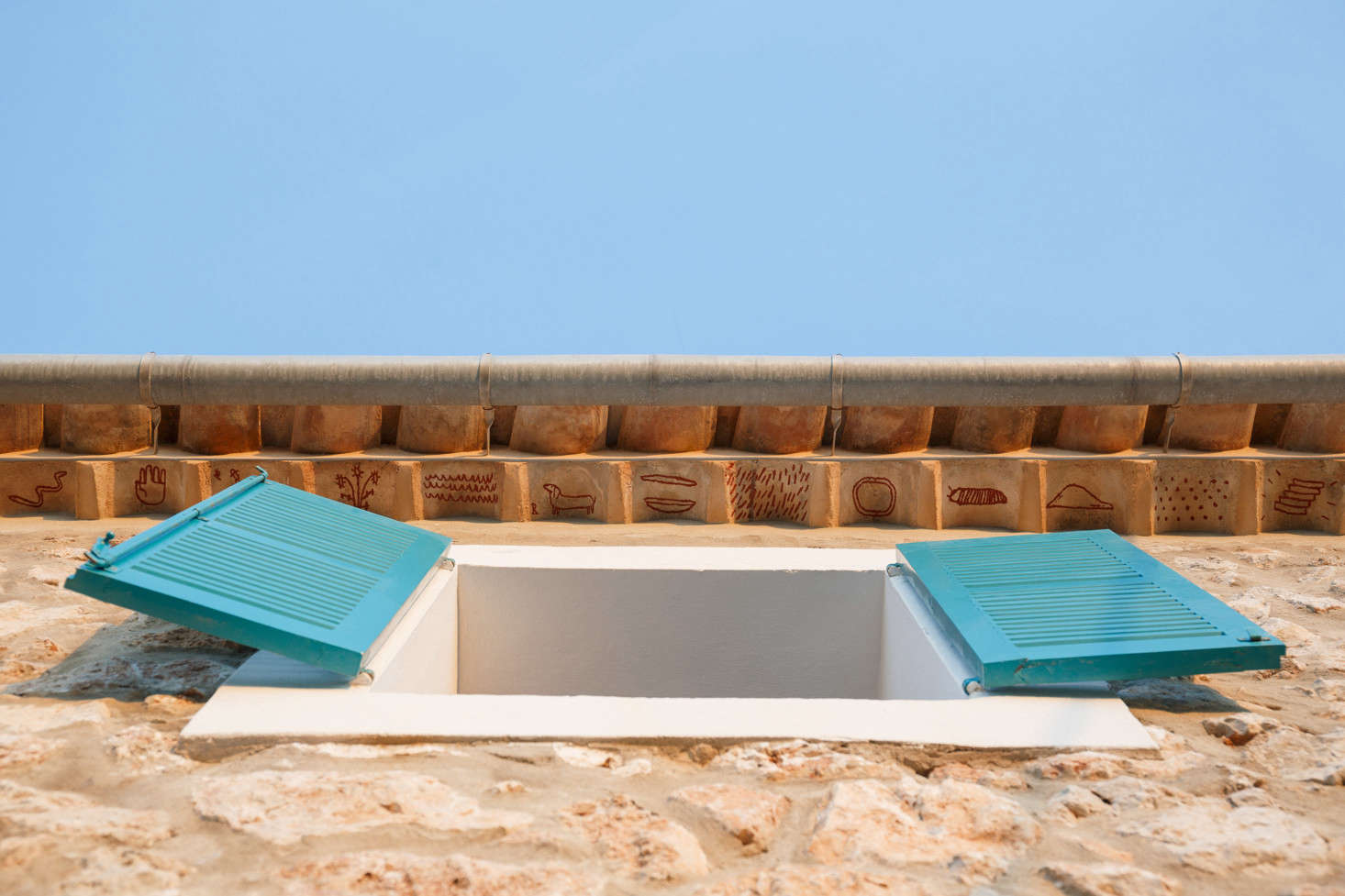 In another nod to Mallorcan tradition, the architects hired artist Luis Urculo to paint small rust-colored symbols beneath the roof tiles—a play on the medieval tradition of teules pintades, said to protect the inhabitants of the house. Of the bright shutters, the architects say, “The traditional color for blinds in this part of the island is mainly green and also blue, so we choose something in the middle that we liked.”