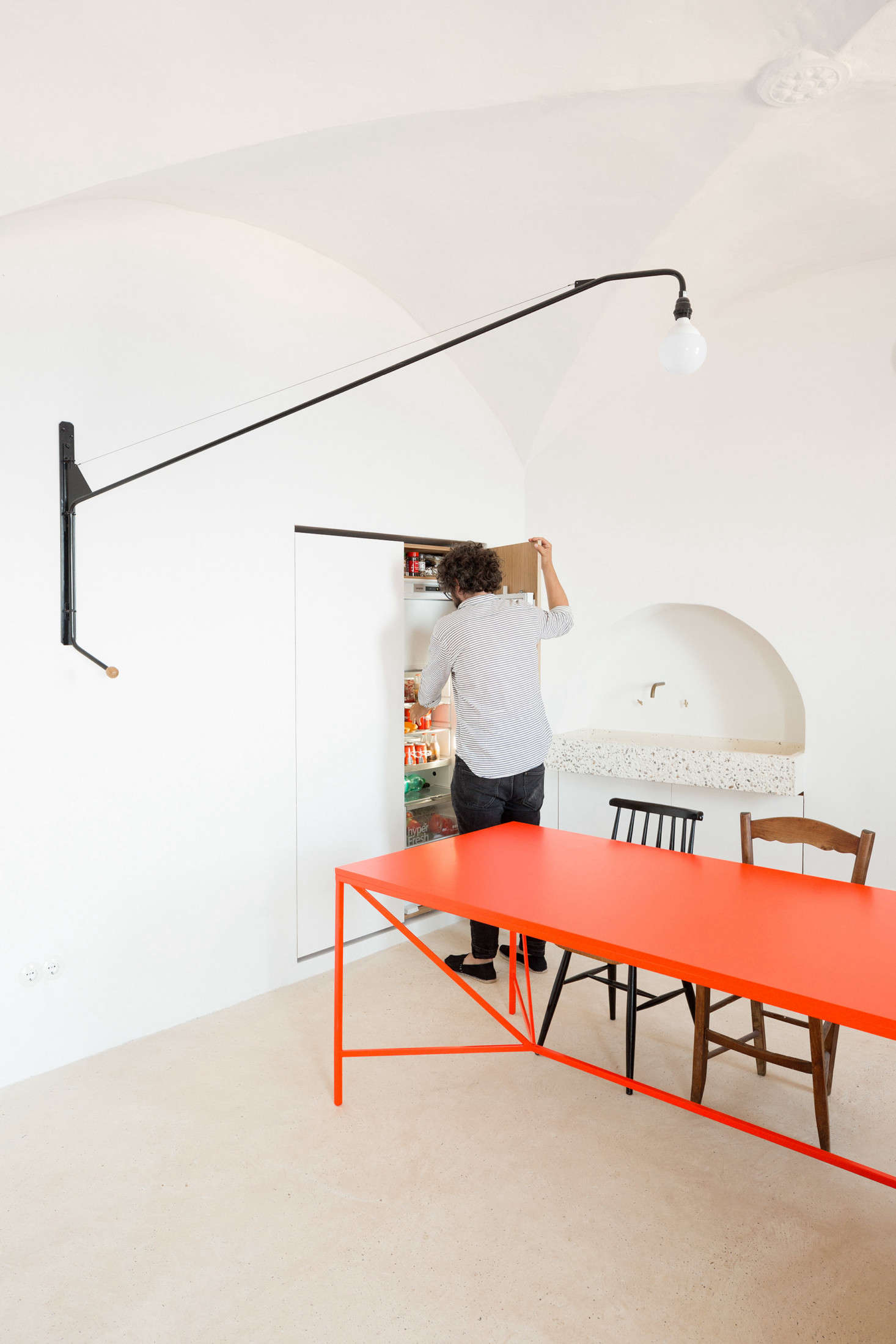 To the left of the dining table, the architects enlarged an existing niche to fit—behind the righthand door—a fridge and freezer and—behind the lefthand door—a washing machine, electric oven, and food storage. “We decided to design the flashed doors as invisible as possible, so we put an integrated fridge and managed to avoid having any door handle,” the architects say. “We just left the gap at the top to open the door and for ventilation.” The niche is deep enough to allow for proper ventilation behind the appliances.