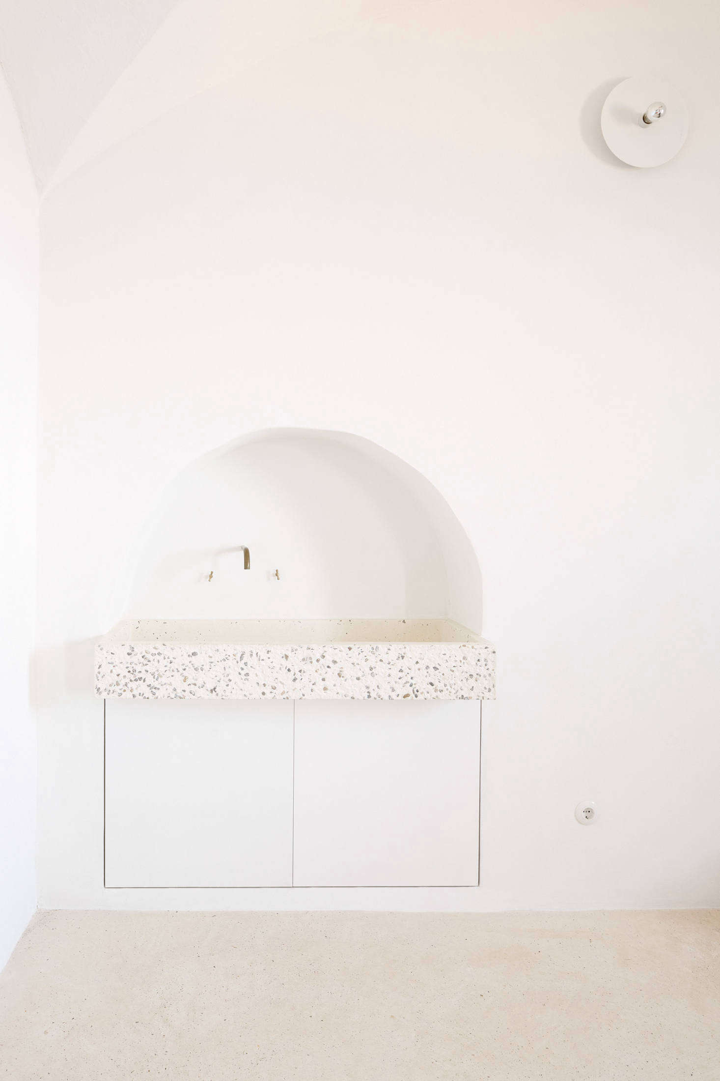 Palencia and Colón preserved a small archway in the kitchen and installed a custom tinted-concrete sink by local company Huguet, a reference to Mallorcan stone sinks. Two cabinets underneath store cleaning products and house the waste bin. Of the subtle white light overhead, the architects say: “It’s a lamp designed in 1976 by Georg Gisel for Lehni, a Swiss furniture company that also produces an aluminum furniture series by Donald Judd, among others. It’s a simple round white aluminum plate hosted in a standard ceramic lamp holder.”