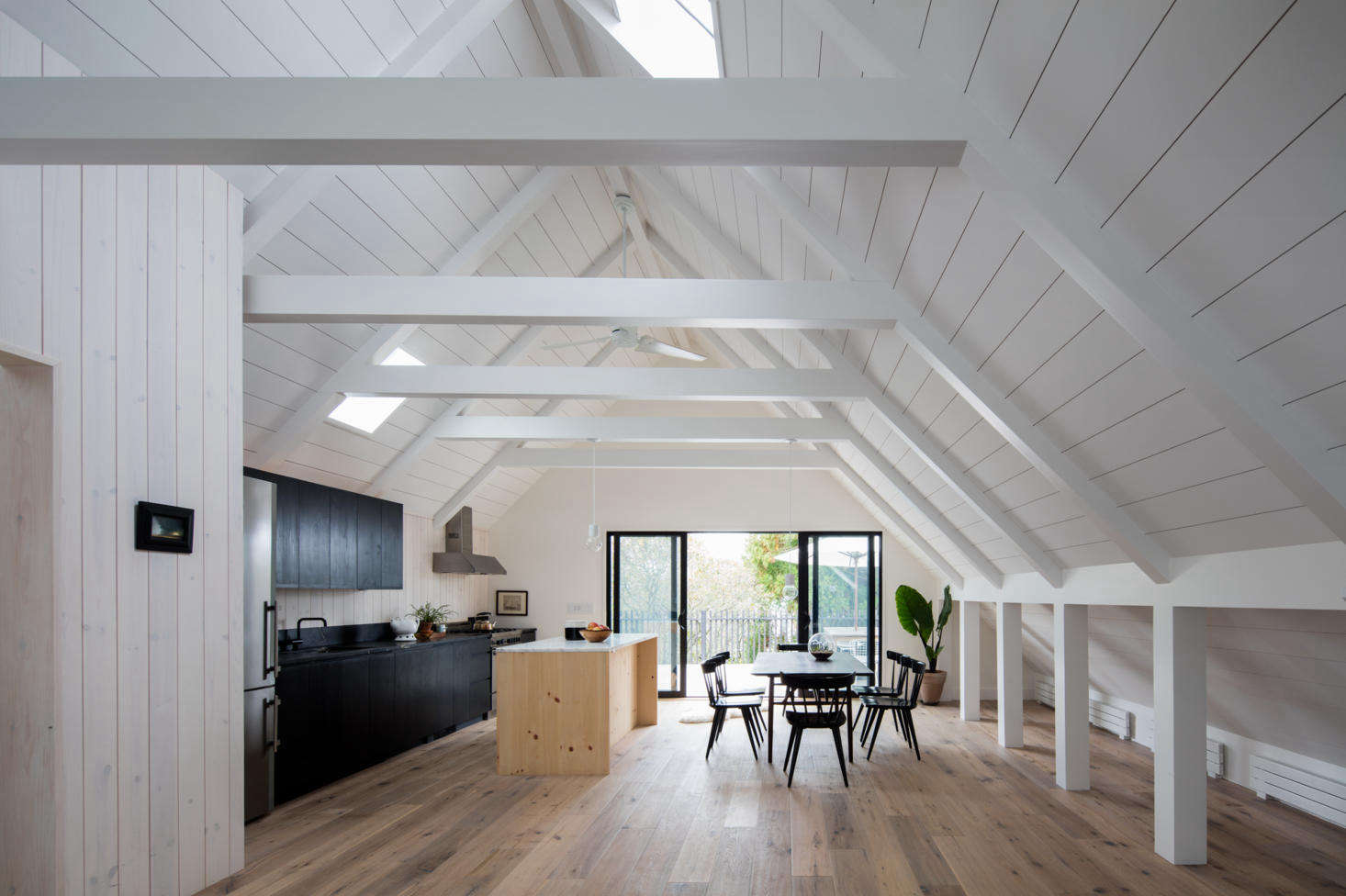 On the open-plan top floor, the kitchen countertops are soapstone, and the heart pine island has countertops of statuary marble. On the far right, flat-panel baseboard radiators by Runtal heat the space.