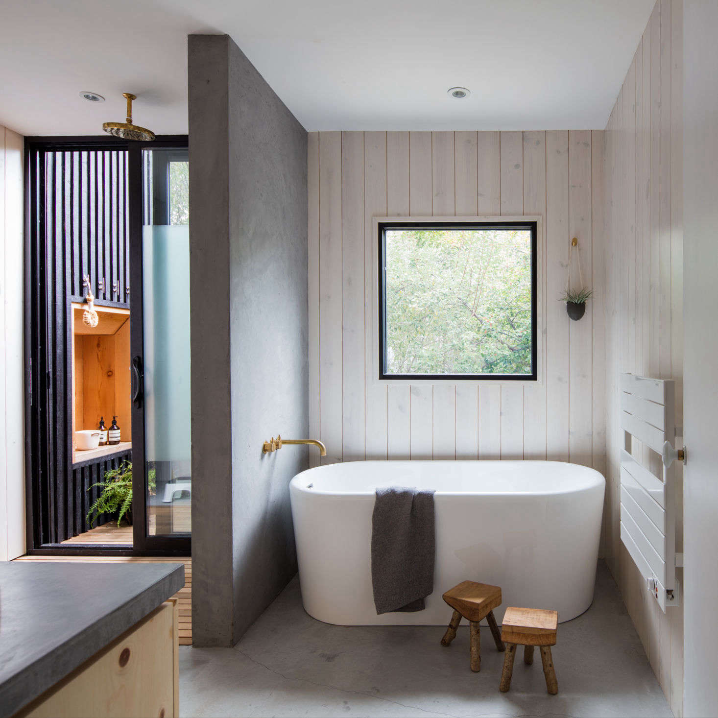 A wall of rendered concrete plaster splits the shower from the bathtub. The concrete floors have radiant underfloor heating, and a towel warmer hangs on the wall by the bath.