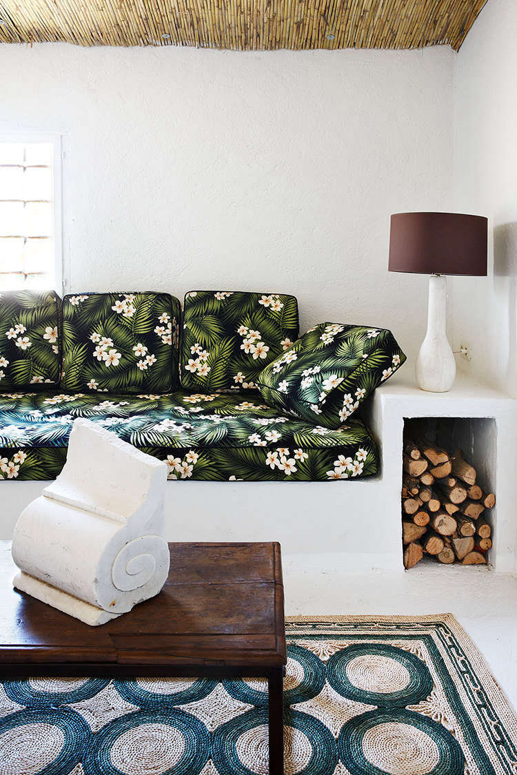 On one end of the room, an example of Castella’s eclectic style: a built-in bench serves as both lounge space (with cushions upholstered in vintage floral fabric, found in Hawaii) and log storage for the nearby fireplace. An architectural remnant becomes sculpture on the low table.