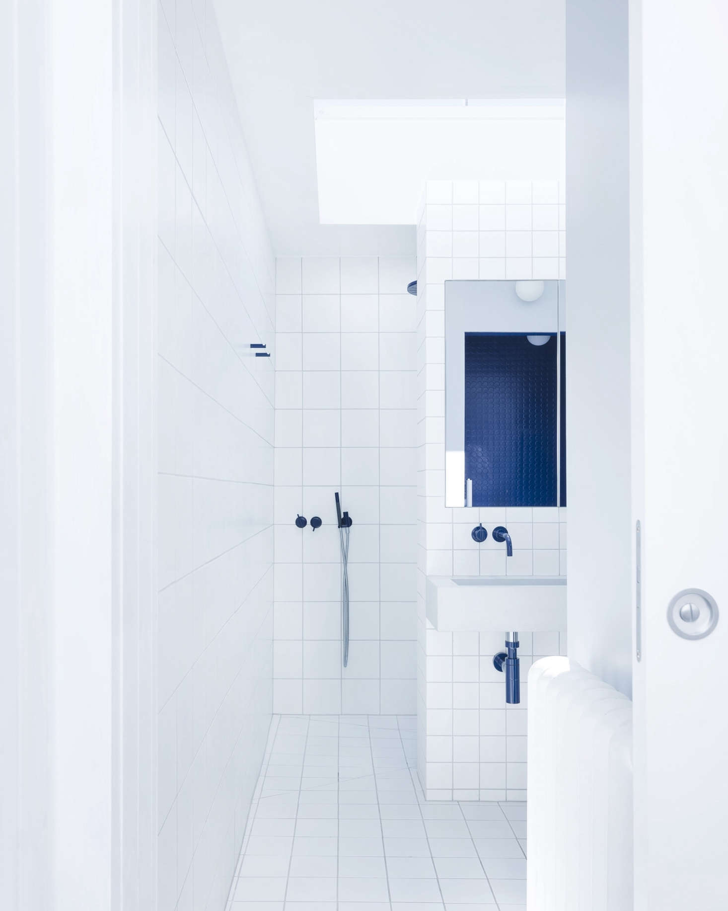 The en-suite blue-and-white master bath makes use of standard white tile in three sizes: the smallest on the sink wall, medium on the floor, and the largest on the central wall, all with gray grout.