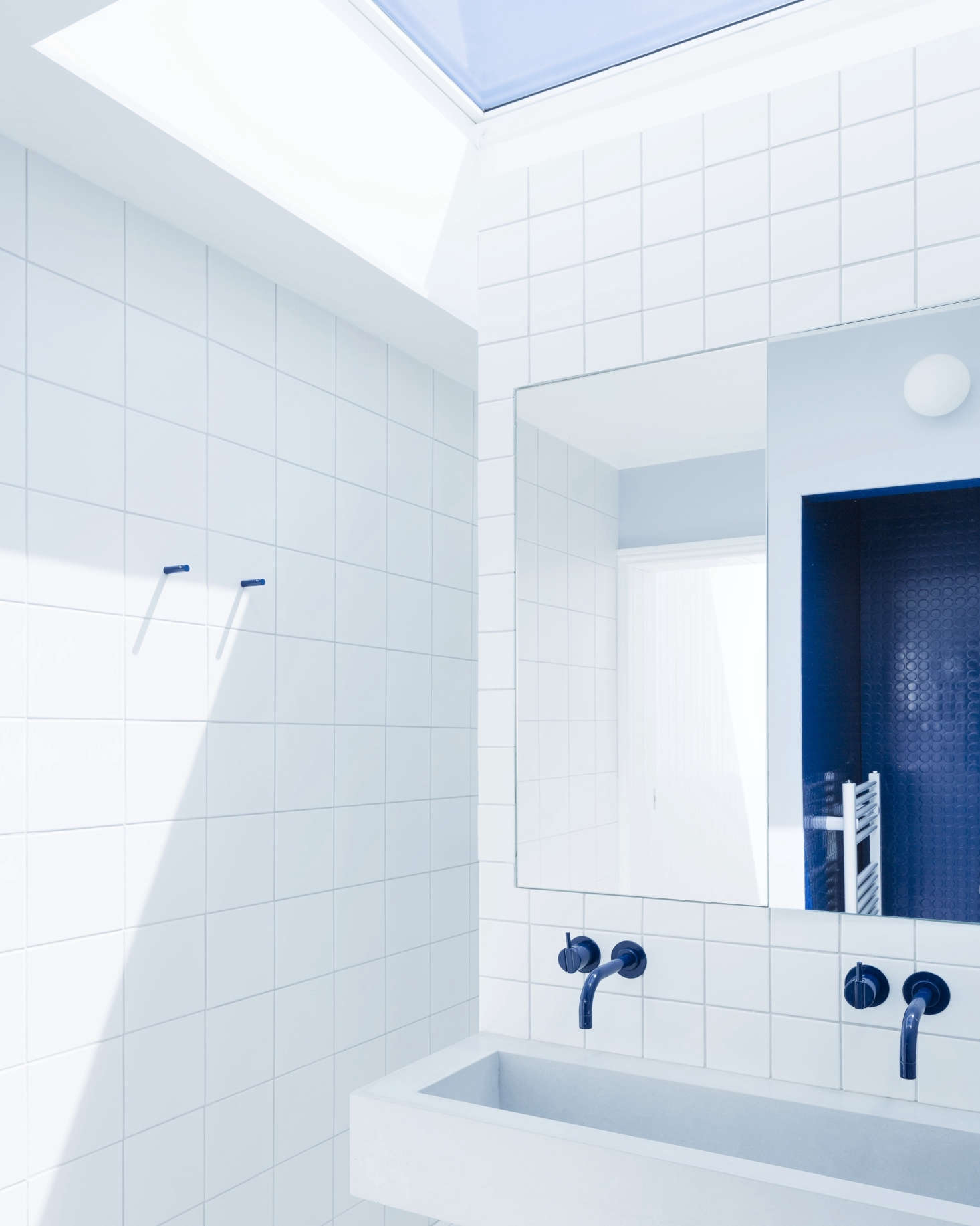 The room is divided into two halves by a tiled walk-around wall with a cast concrete sink made by the contractor, who also fabricated the medicine cabinets (reflected in the right is the WC clad in royal blue rubber flooring).
