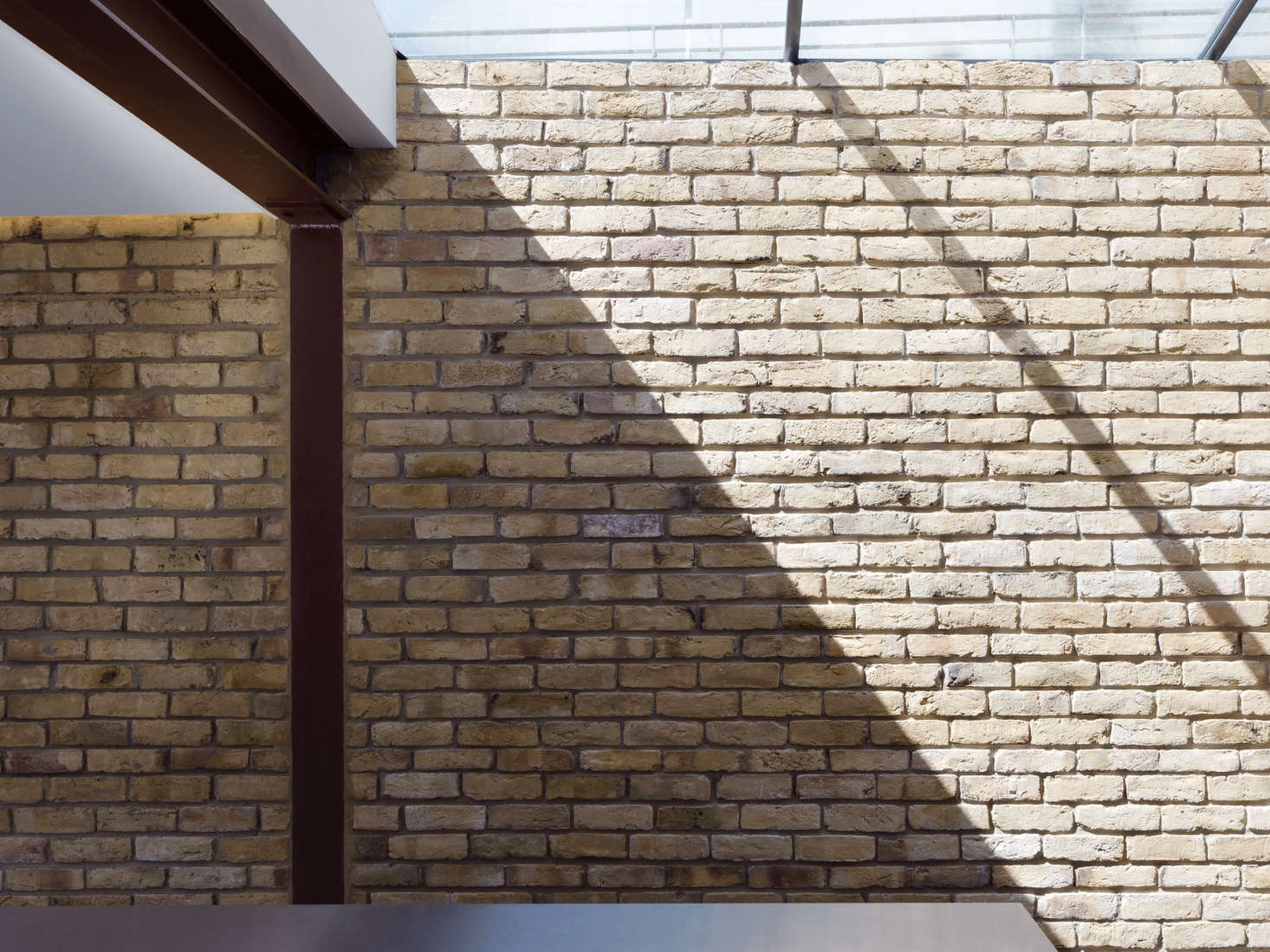 In the kitchen, a wall of reclaimed London stock brick matches the brick on the exterior. The new structure has exposed steel supports and I-beams that are spray-painted burgundy. Also note the 