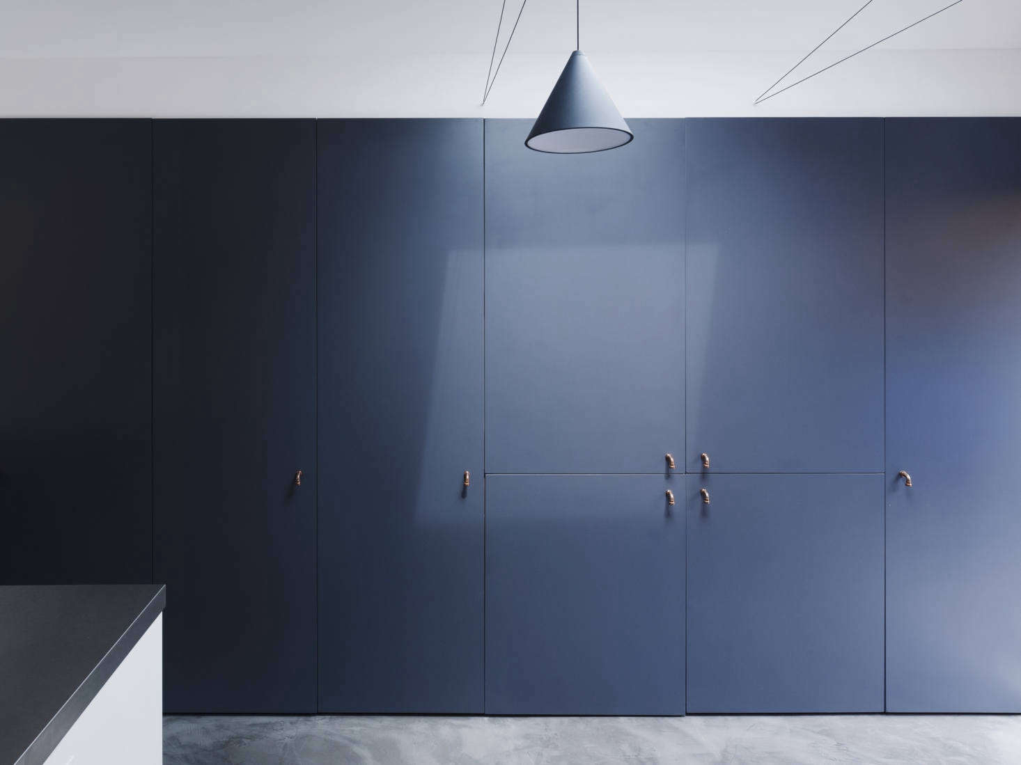 The refrigerator is concealed on the storage wall, which has door pulls made from bent copper plumbing pipes.