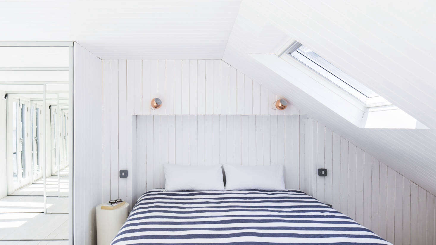 The whitewashed paneling continues in the under-the-eaves master bedroom, which integrates one of the roof extensions. A recess in the paneling takes the place of a headboard.
