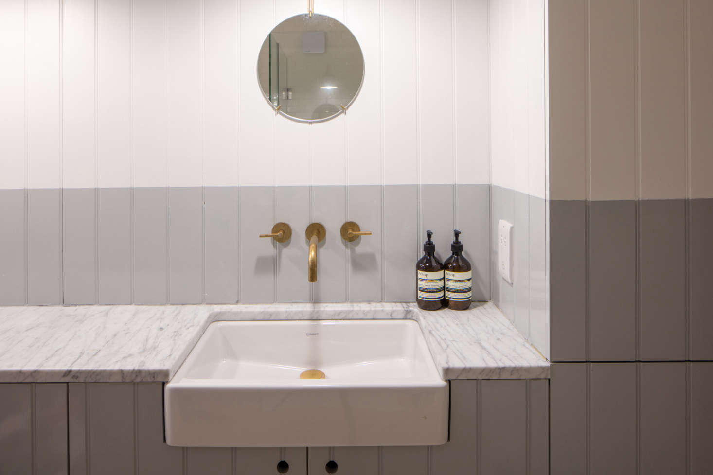 A bathroom is small but luxe with a marble counter. It’s half-painted in Pure Grey 2 from Papers & Paints.