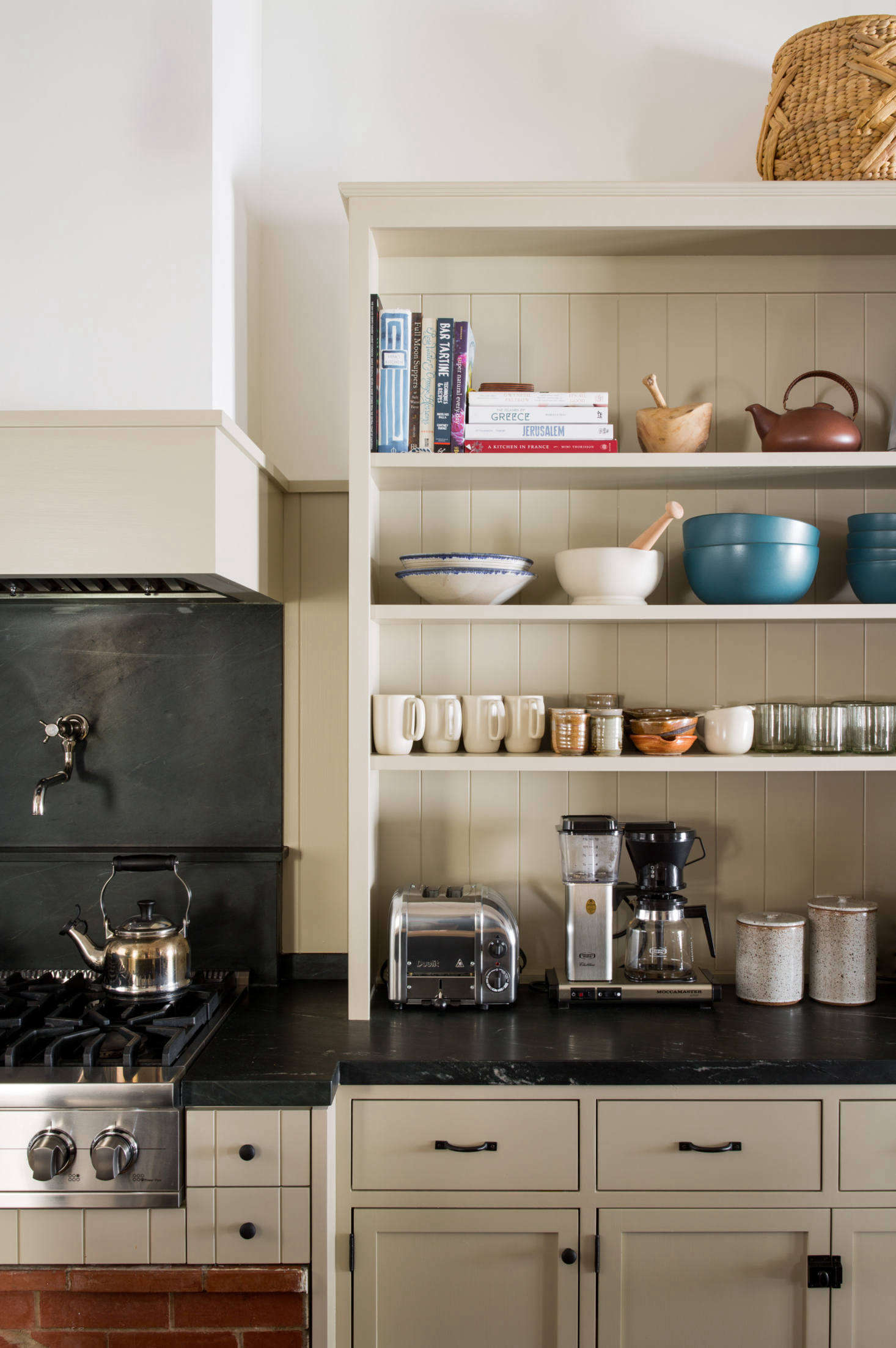 The custom cabinets have V-groove fronts that match the wainscoting and the original cladding elsewhere in the house. (For more, consult The Ultimate Wood Paneling Guide.) Above the stove is a pot filler by Waterworks and a Le Creuset kettle. The toaster is Dualit’s two-slice chrome version.