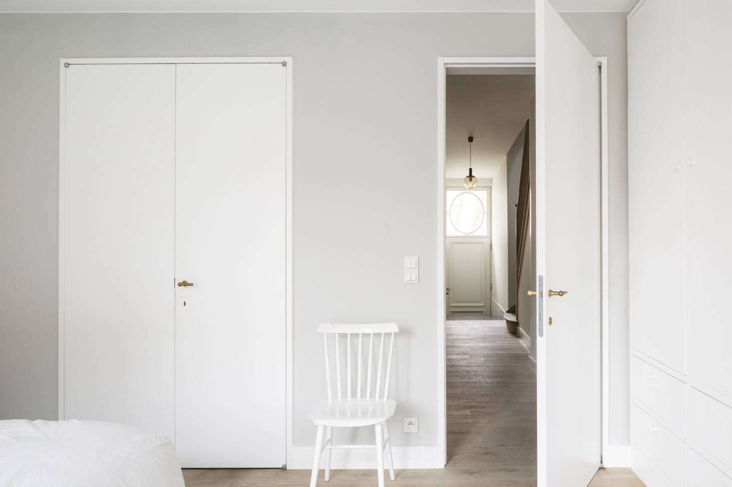 On the ground floor, one flight down, is the master bedroom, set back from the street for maximum privacy. It’s painted in a pale gray, with subtle brass hardware from family-owned Belgian company Jaro Style, which the architects used throughout, and a white ladder-back chair from Dille & Kamille.