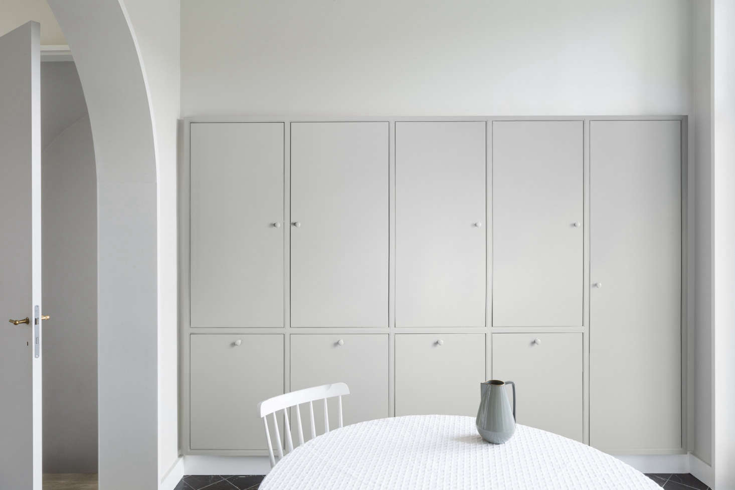 Opposite, inset cabinetry makes use of the space behind the wall (which, toward the front of the townhouse, is where the staircase is set). Kitchen appliances, including an oven and fridge, plus a vacuum, are hidden away neatly within the cupboards.
