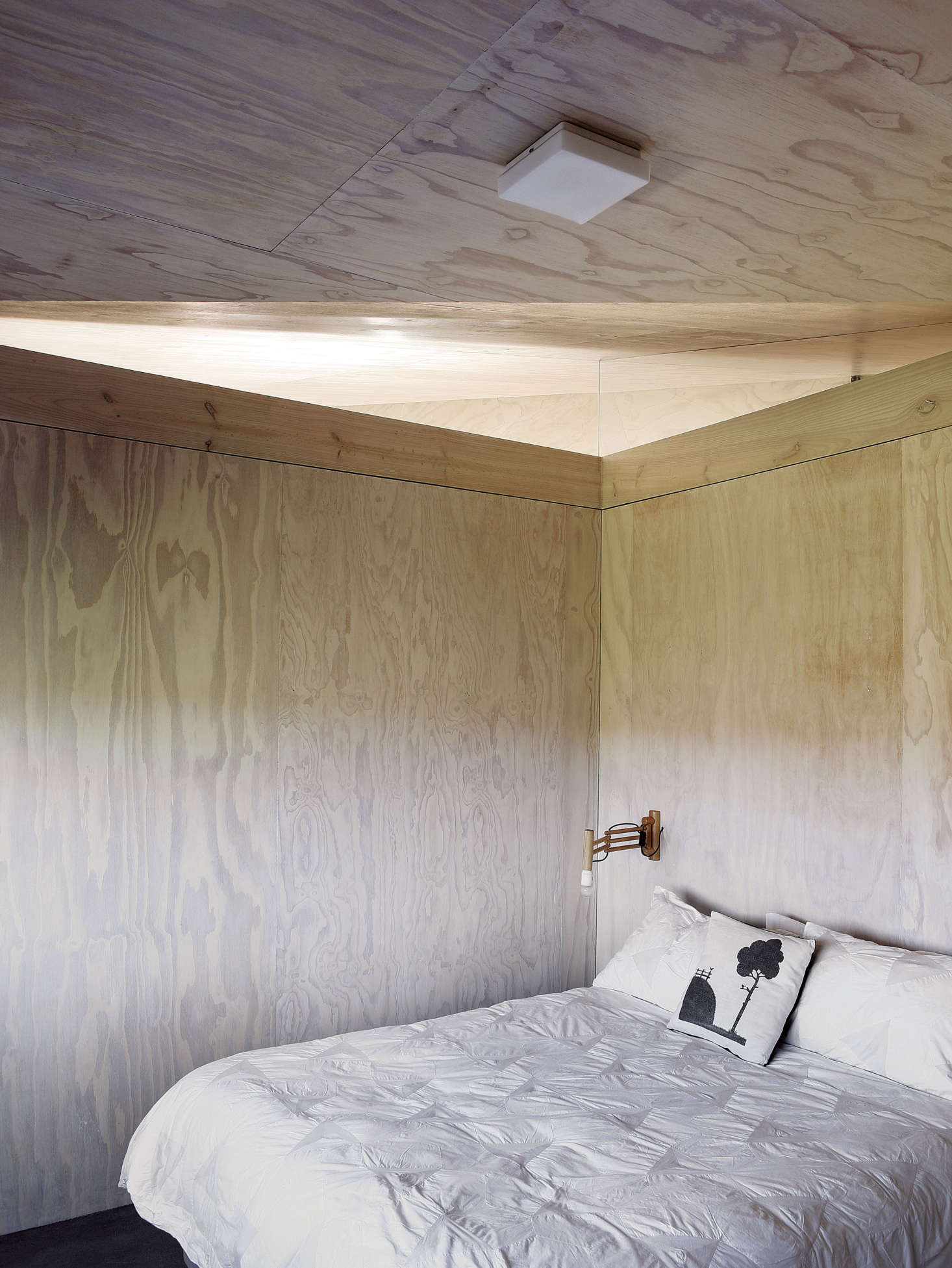 A guest bedroom is kept spare with a ceiling-mount light and vintage wood sconce.