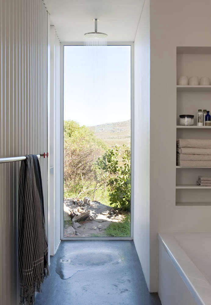 The shower in the bathhouse is partially outdoors (through the doorway to the left) with a Grohe Rainshower Cosmopolitan 210 Shower Head and red plumbing valves. The bathroom floors are sealed cement screed.