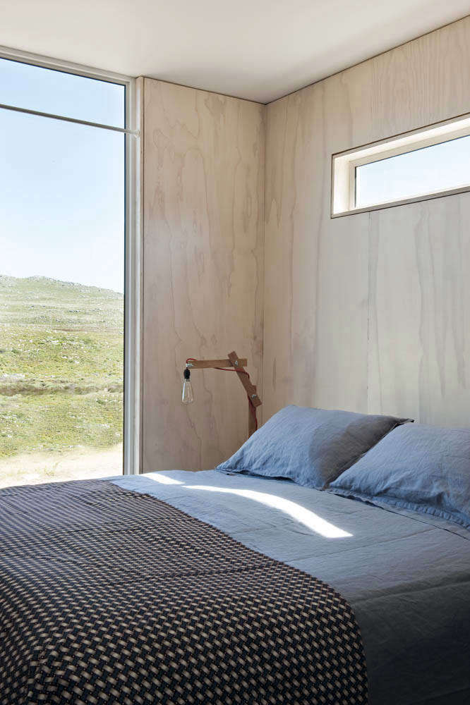 The master bedroom overlooks sweeping views of the nature reserve. The blue linen sheets and patterned cover are from Country Road (no longer available) and the bedside light is a vintage 1950s Danish table lamp.