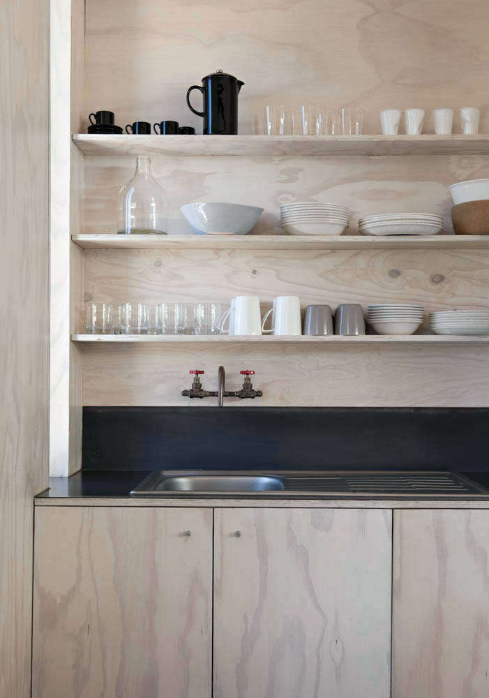 The architects enlisted a boat builder to work on the plywood joinery throughout the house, including the compact kitchen, which was designed on a budget and has countertops and a backsplash made of mild steel that was heated and hot waxed on-site. The kitchen faucet was also made on-site with plumbing parts.