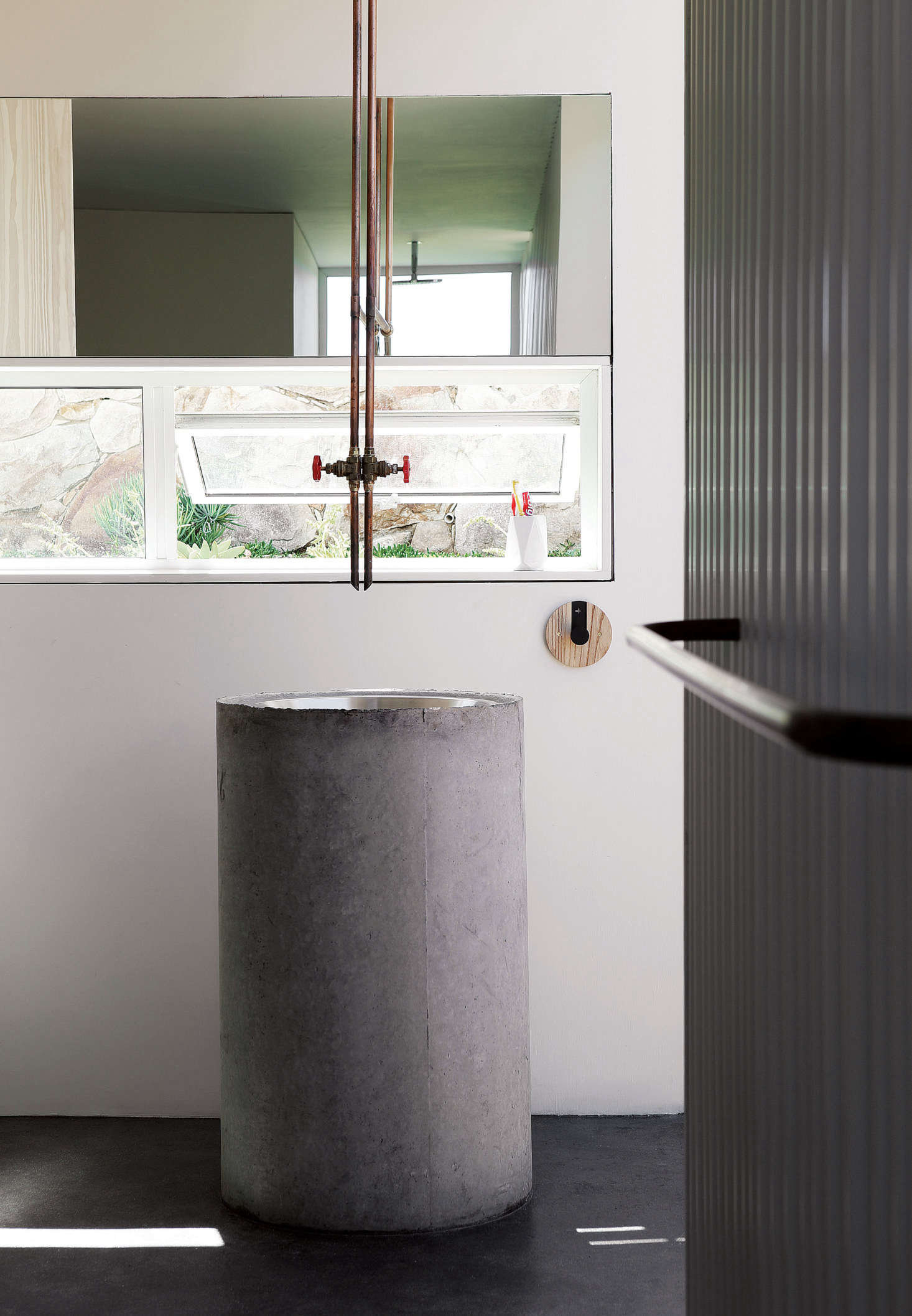 The architects designed the communal “bathhouse” with a large sink made of a stainless steel kitchen prep bowl set into a pre-cast concrete plumbing pipe. The faucet, like the one in the kitchen, is made from copper plumbing pipe.