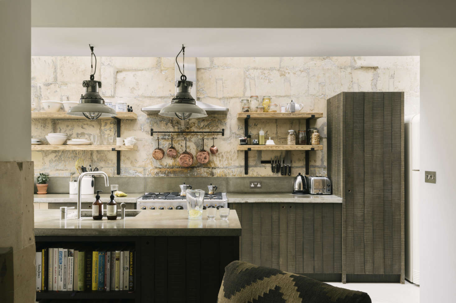 Cookbooks are stored at the front of the island (and the dishwasher and trash bin are on the other side, near the sink). The fridge is just to the right of the tall cabinet, which is used as the pantry and also conceals the microwave.