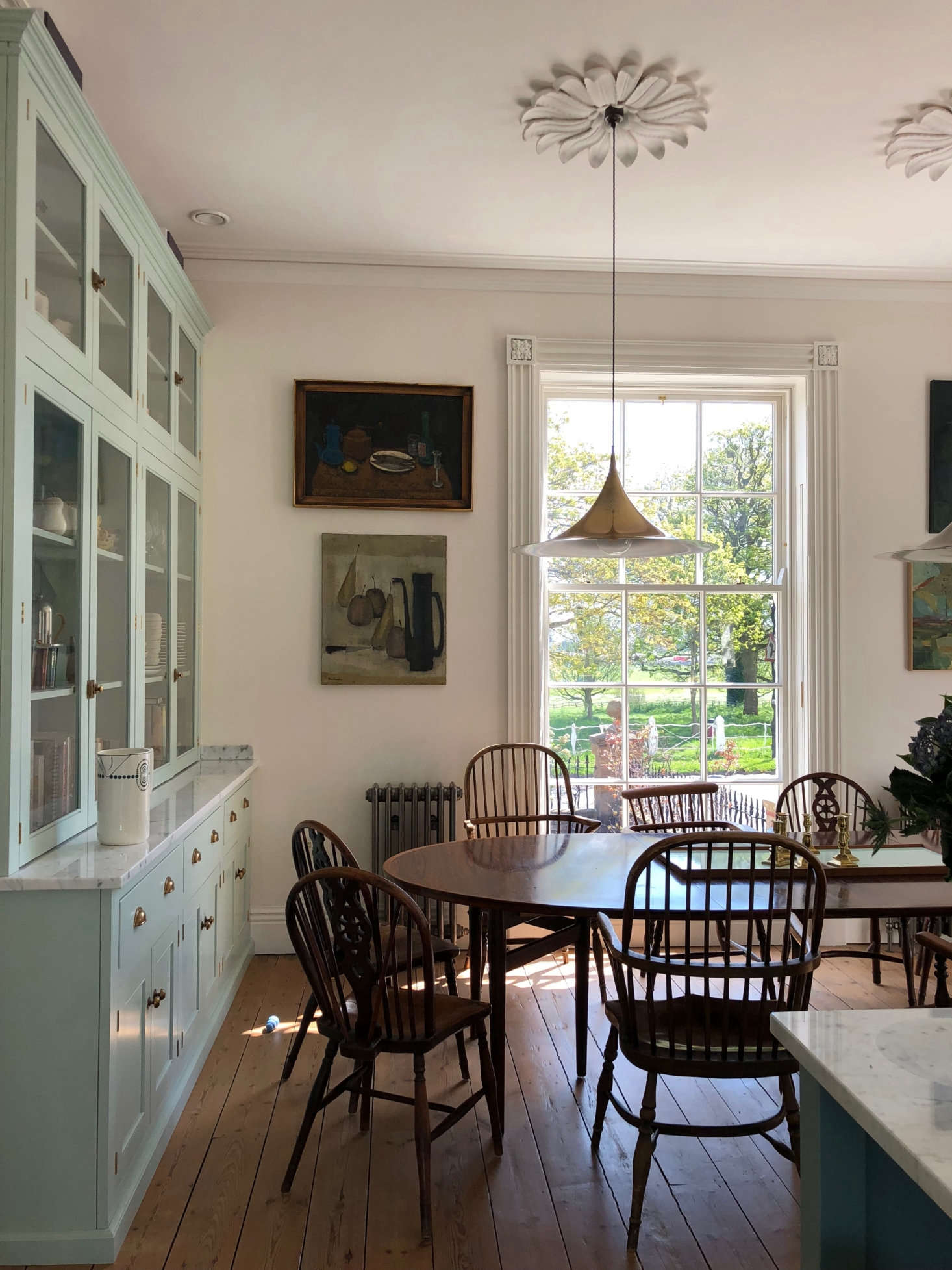 Plaster ceiling roses and a collection of vintage paintings set off the dining area. Though it’s been mistaken for an English antique, our table is actually a Danish modern design by Arne Vodder from Pure Imagination: we wanted a long, not-too-wide oval for the space and it fit the bill. We gathered our antique Windsors in odd lots as the room was finally falling into place. Photograph by Margot Guralnick.